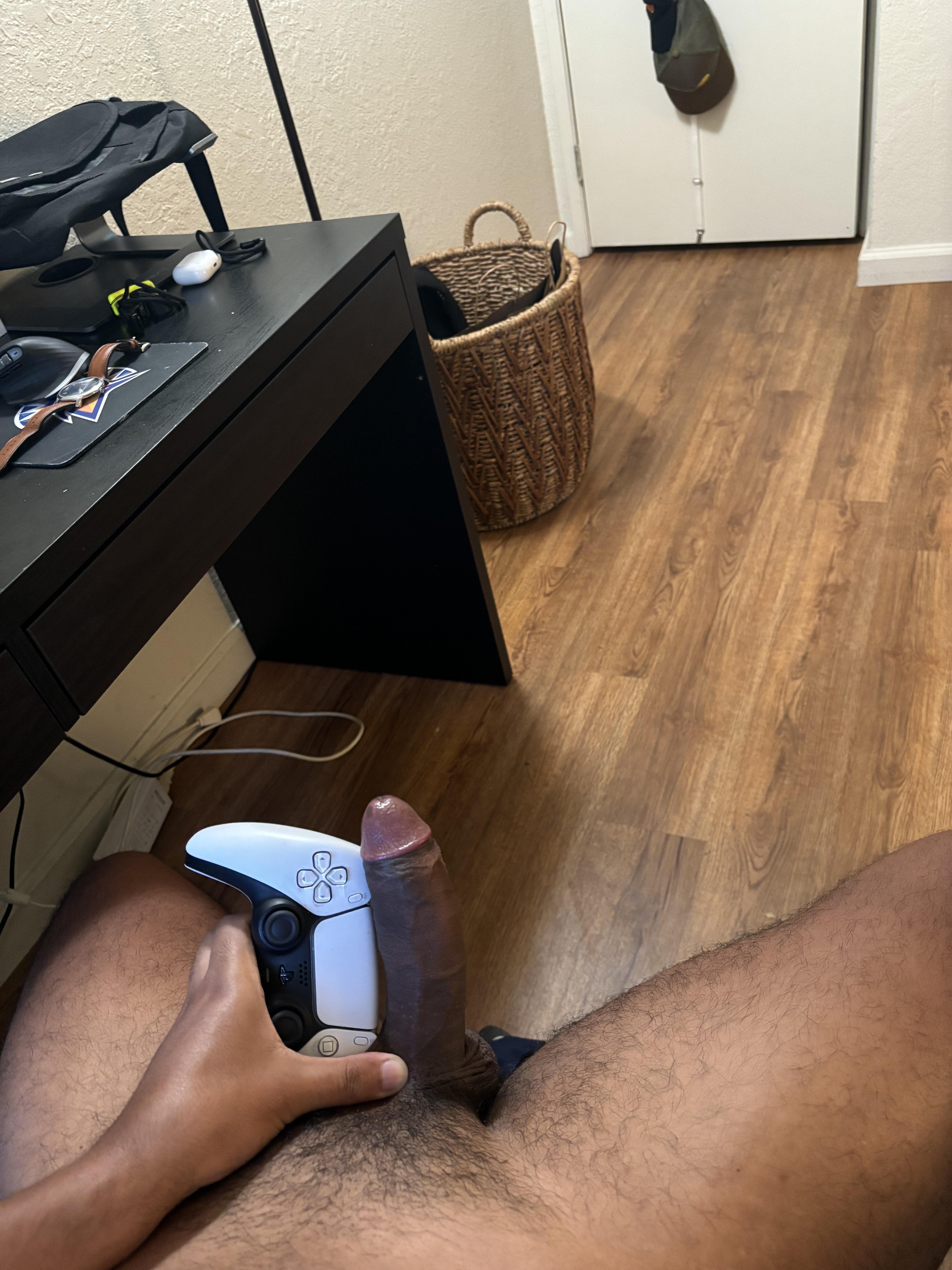 Athletic black man with a huge uncut cock holding a white DualShock 4 controller in a bedroom selfie.