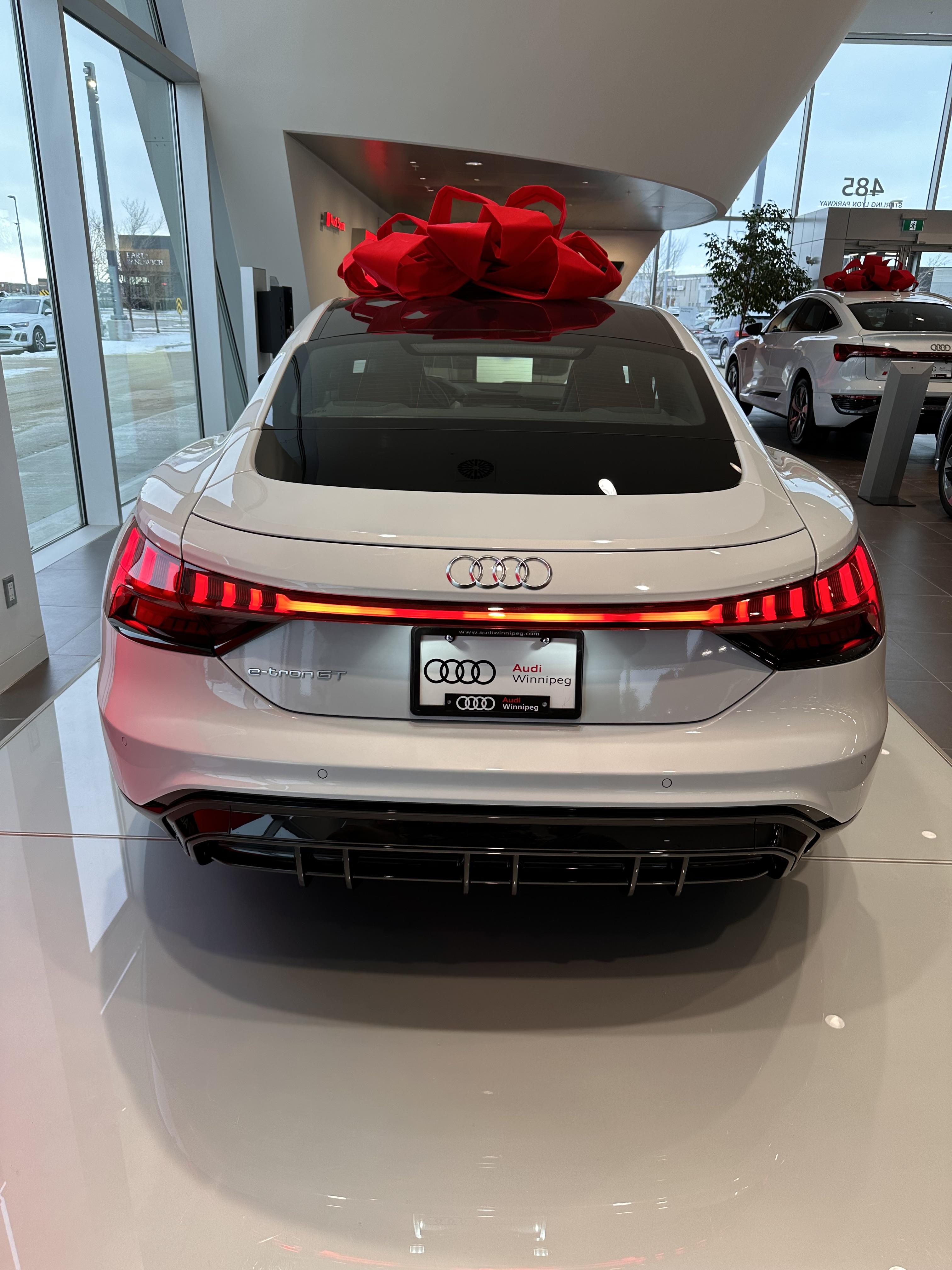 White Audi e-tron GT supercar with a large red bow in an Audi Winnipeg dealership showroom