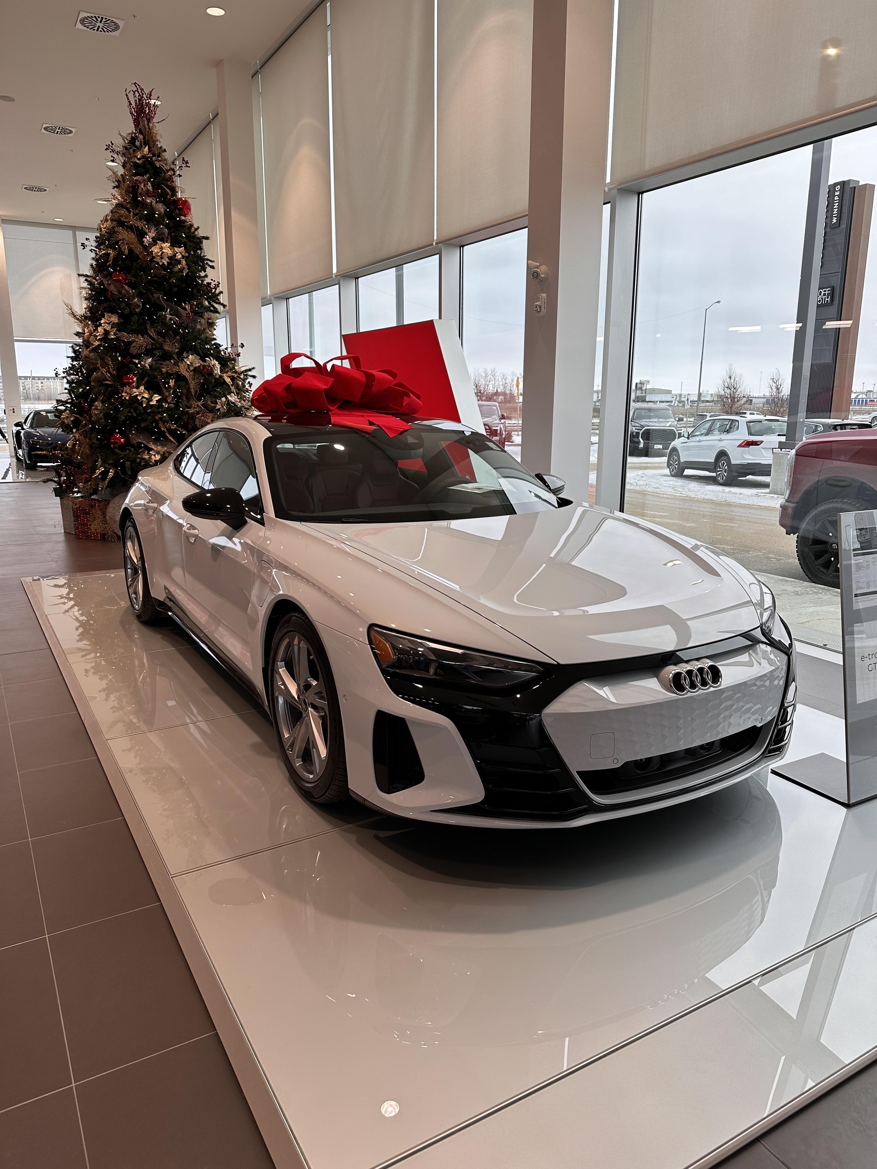 White Audi e-tron GT supercar with a large red bow in an Audi Winnipeg dealership showroom