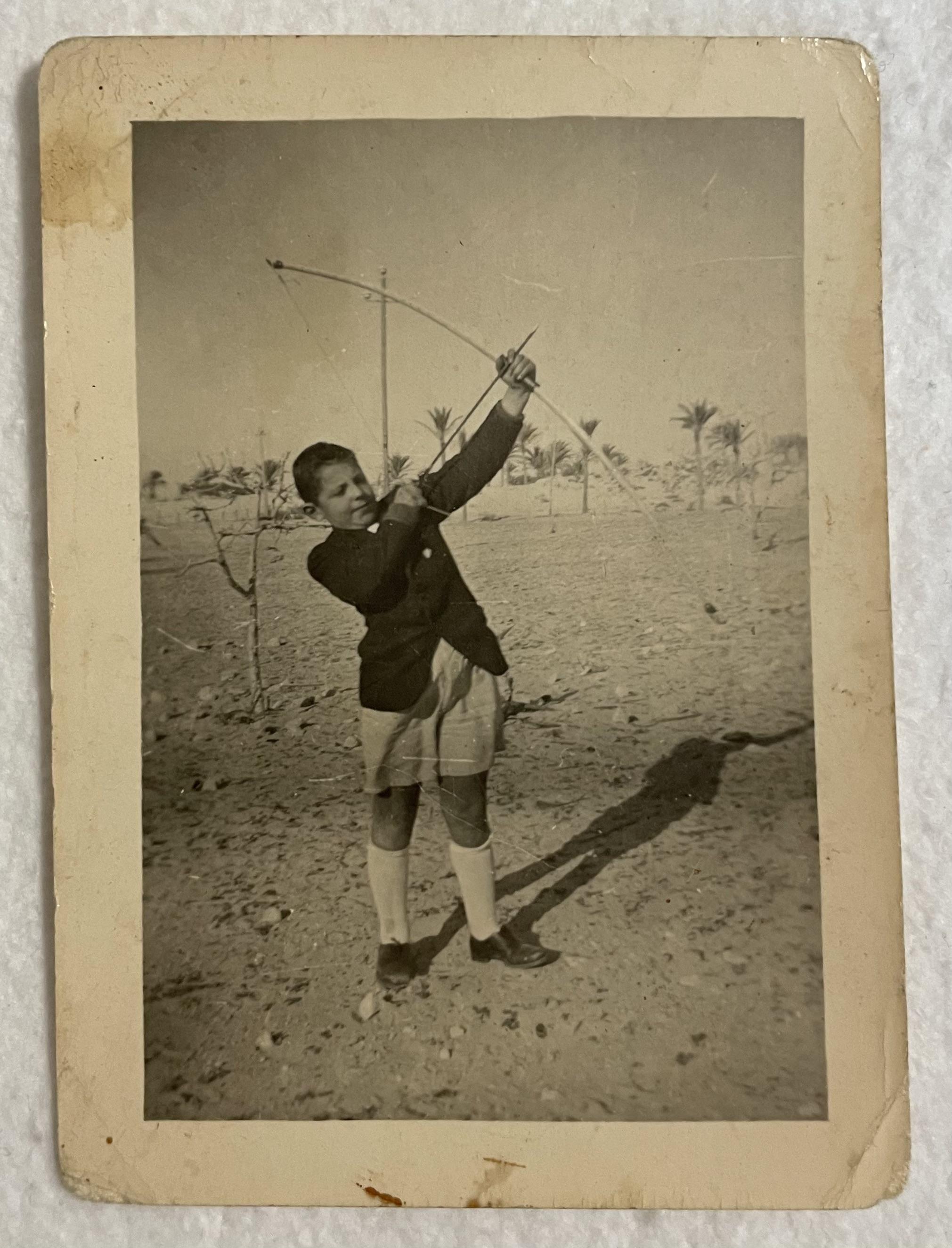A person in a white shirt, hat, and short shorts standing by a wooden wall in a black and white vintage photo.
