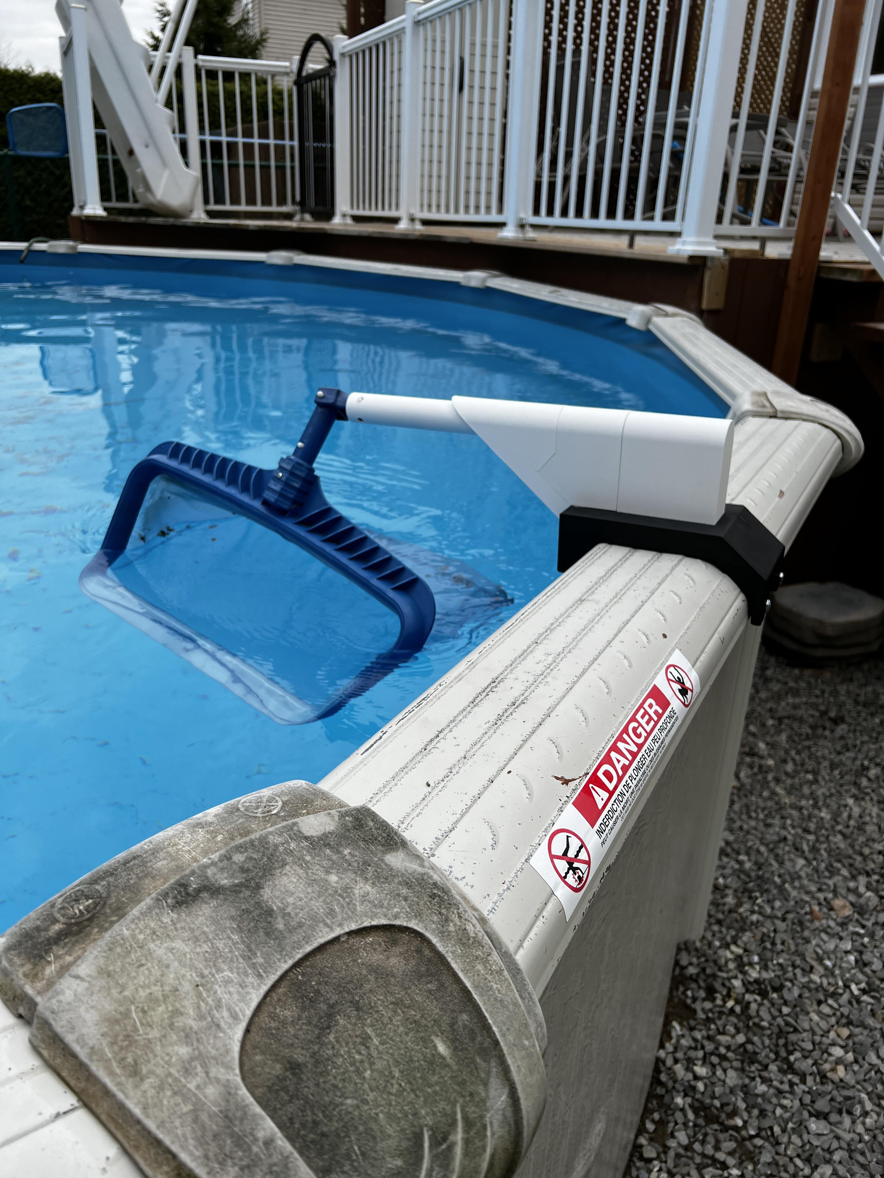 A 3D printed pool leaf skimmer holder attached to the railing of an above-ground swimming pool.