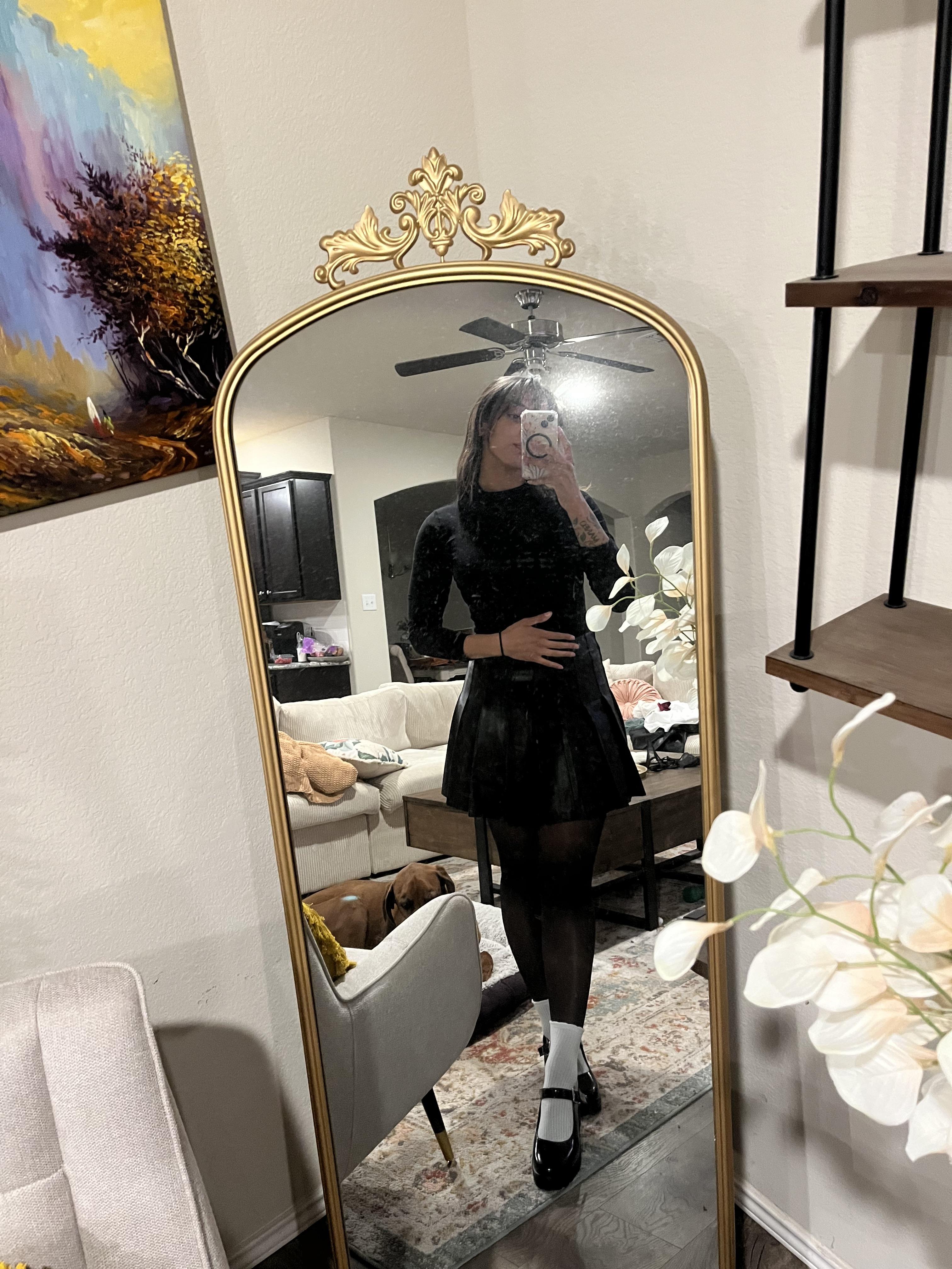 Woman in a pleated leather mini skirt and various white tops and hosiery posing for mirror selfies