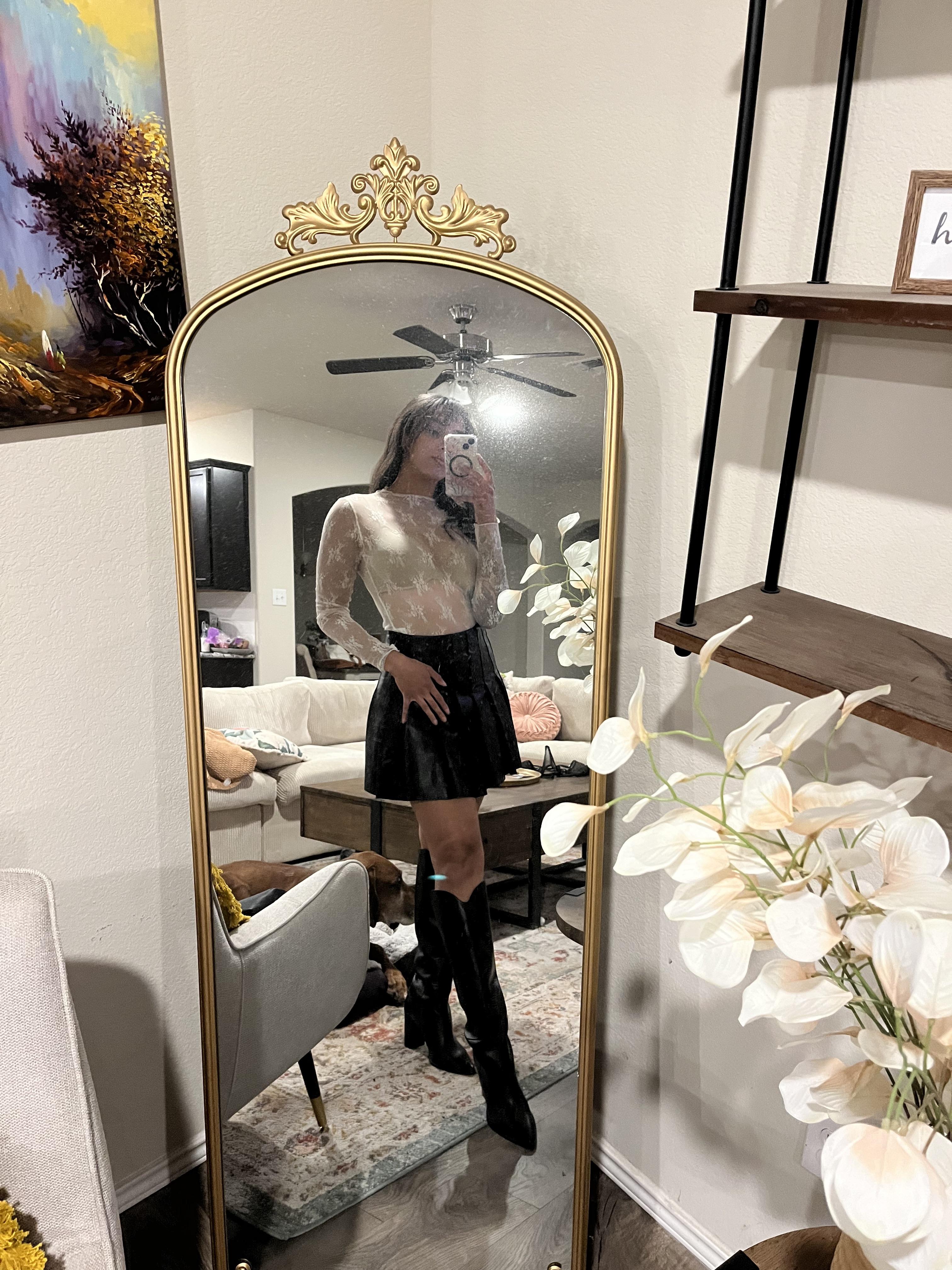 Woman in a pleated leather mini skirt and various white tops and hosiery posing for mirror selfies