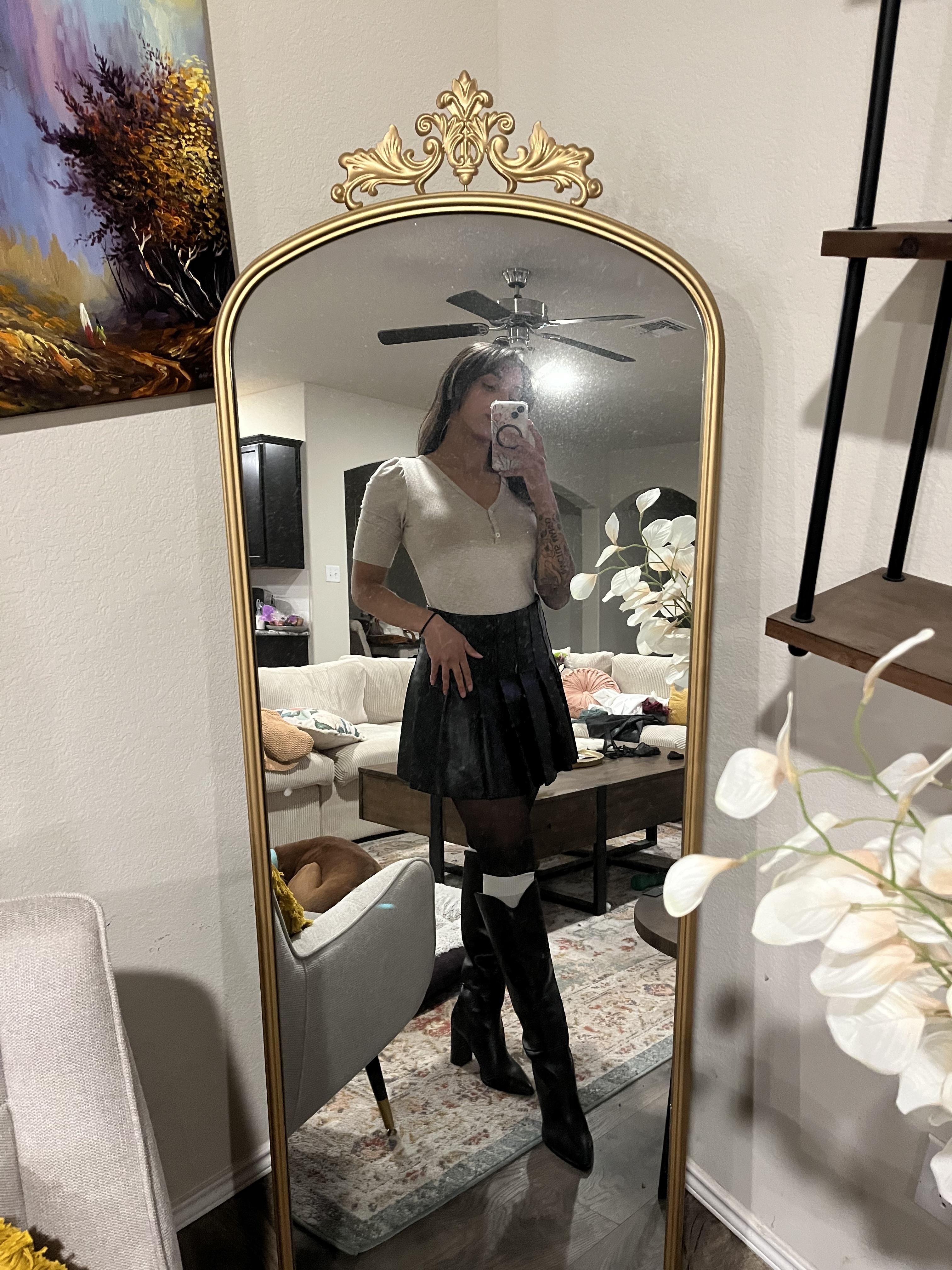 Woman in a pleated leather mini skirt and various white tops and hosiery posing for mirror selfies