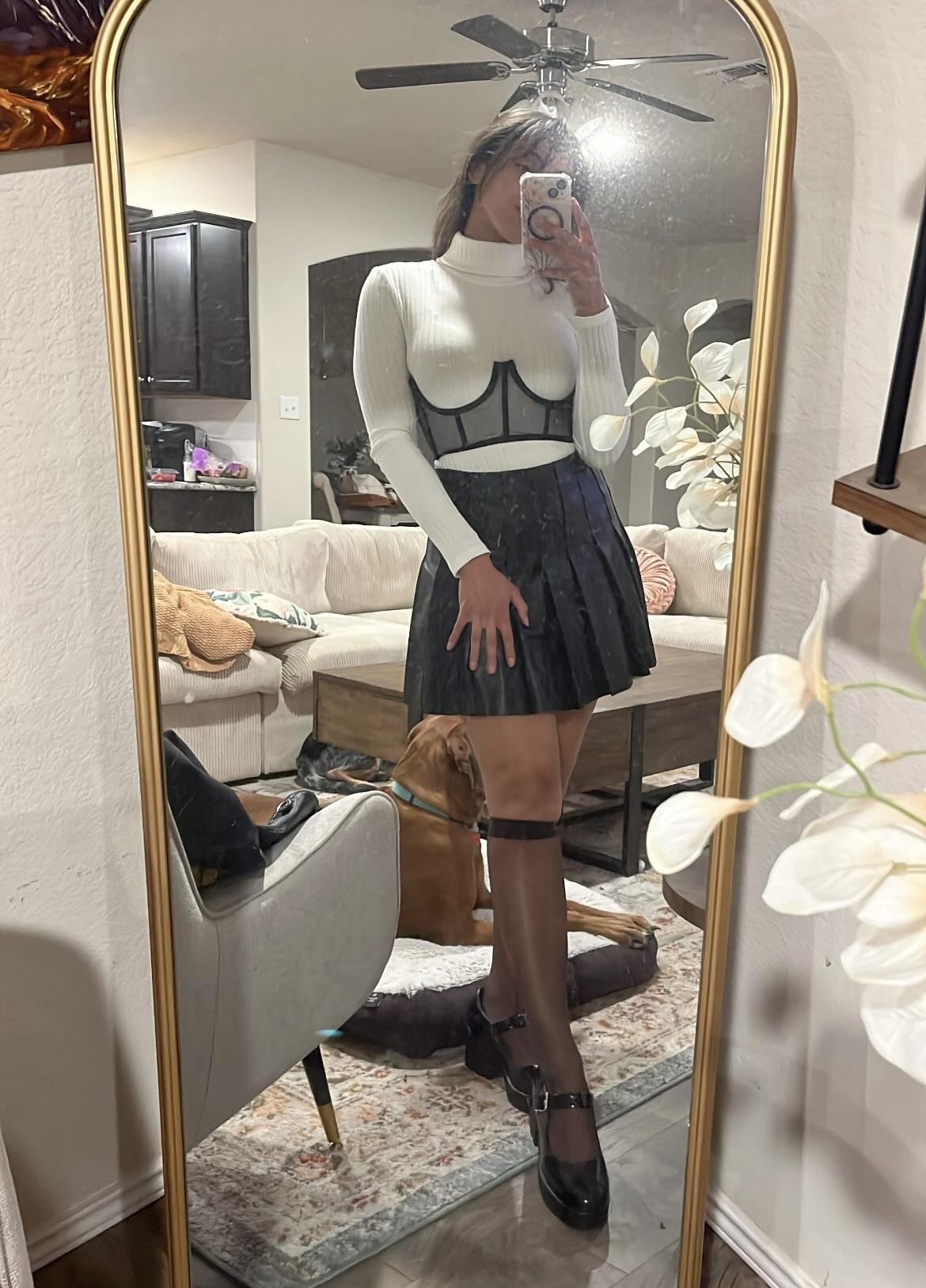 Woman in a pleated leather mini skirt and various white tops and hosiery posing for mirror selfies