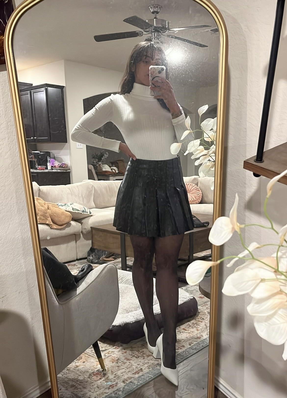 Woman in a pleated leather mini skirt and various white tops and hosiery posing for mirror selfies