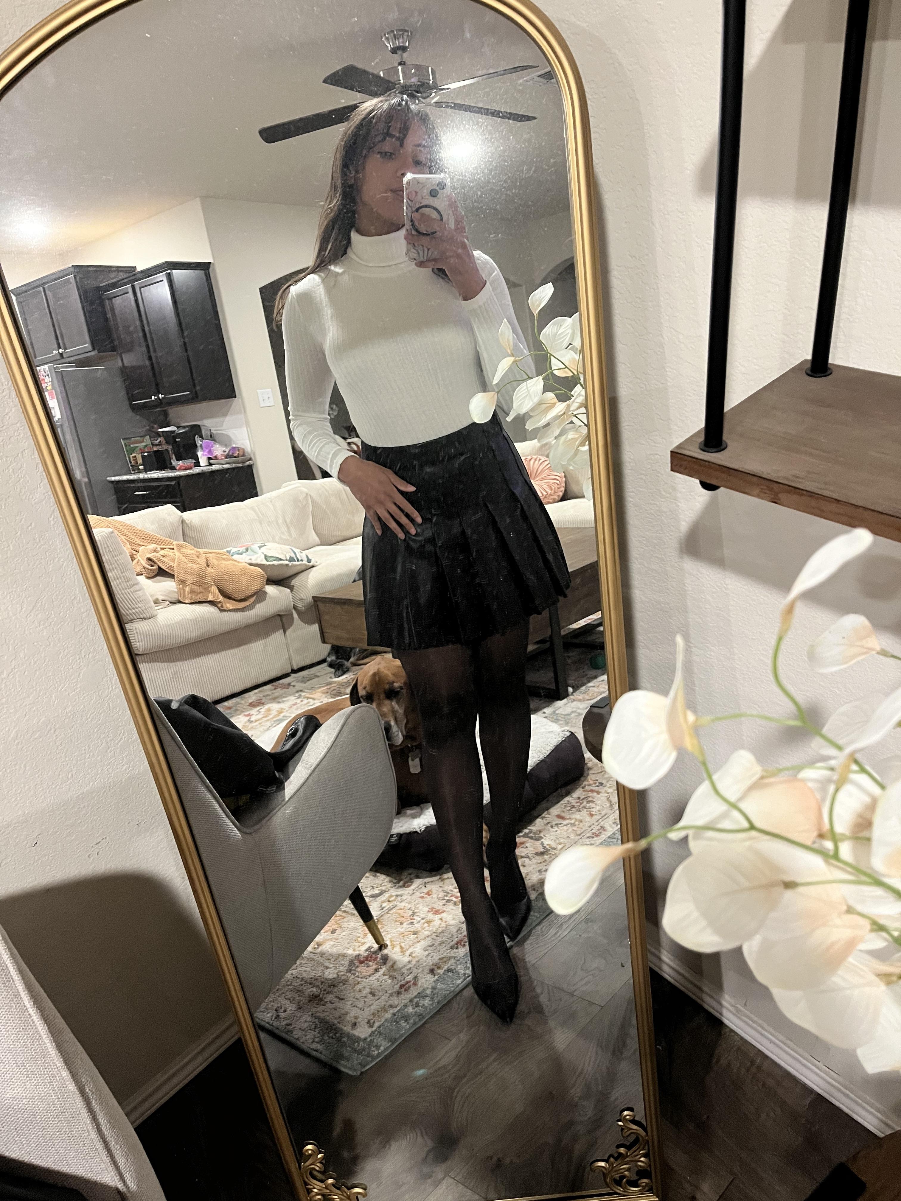 Woman in a pleated leather mini skirt and various white tops and hosiery posing for mirror selfies
