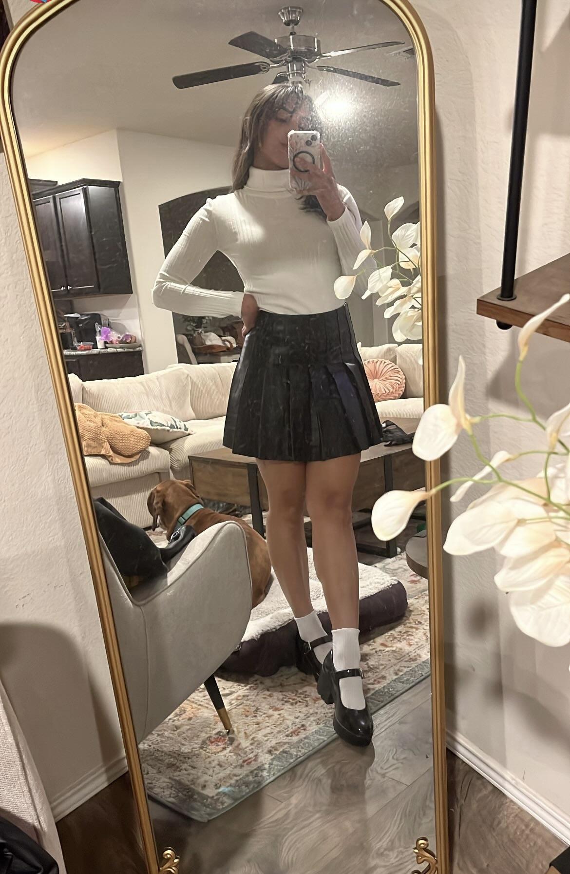 Woman in a pleated leather mini skirt and various white tops and hosiery posing for mirror selfies