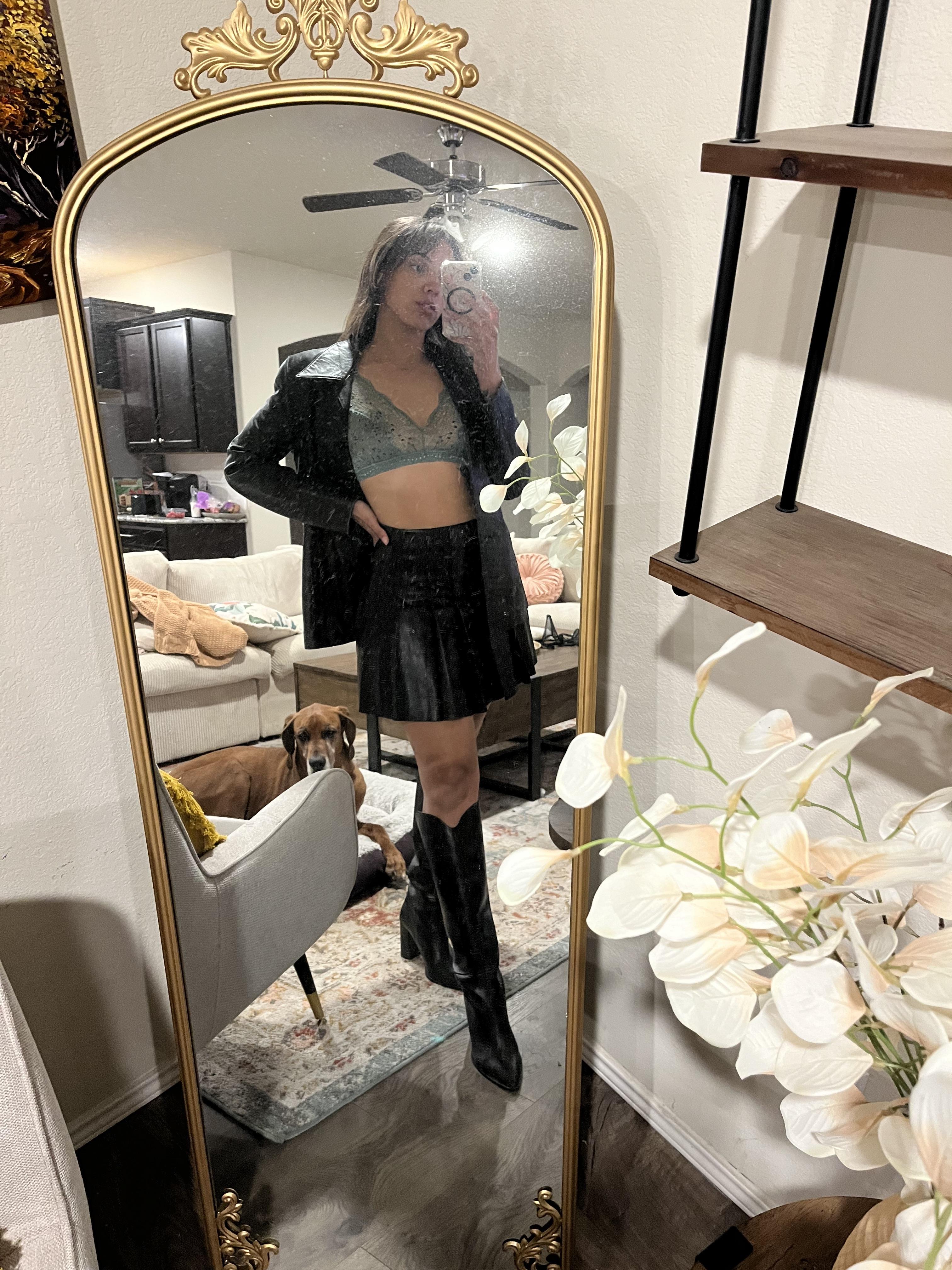 Woman in a pleated leather mini skirt and various white tops and hosiery posing for mirror selfies