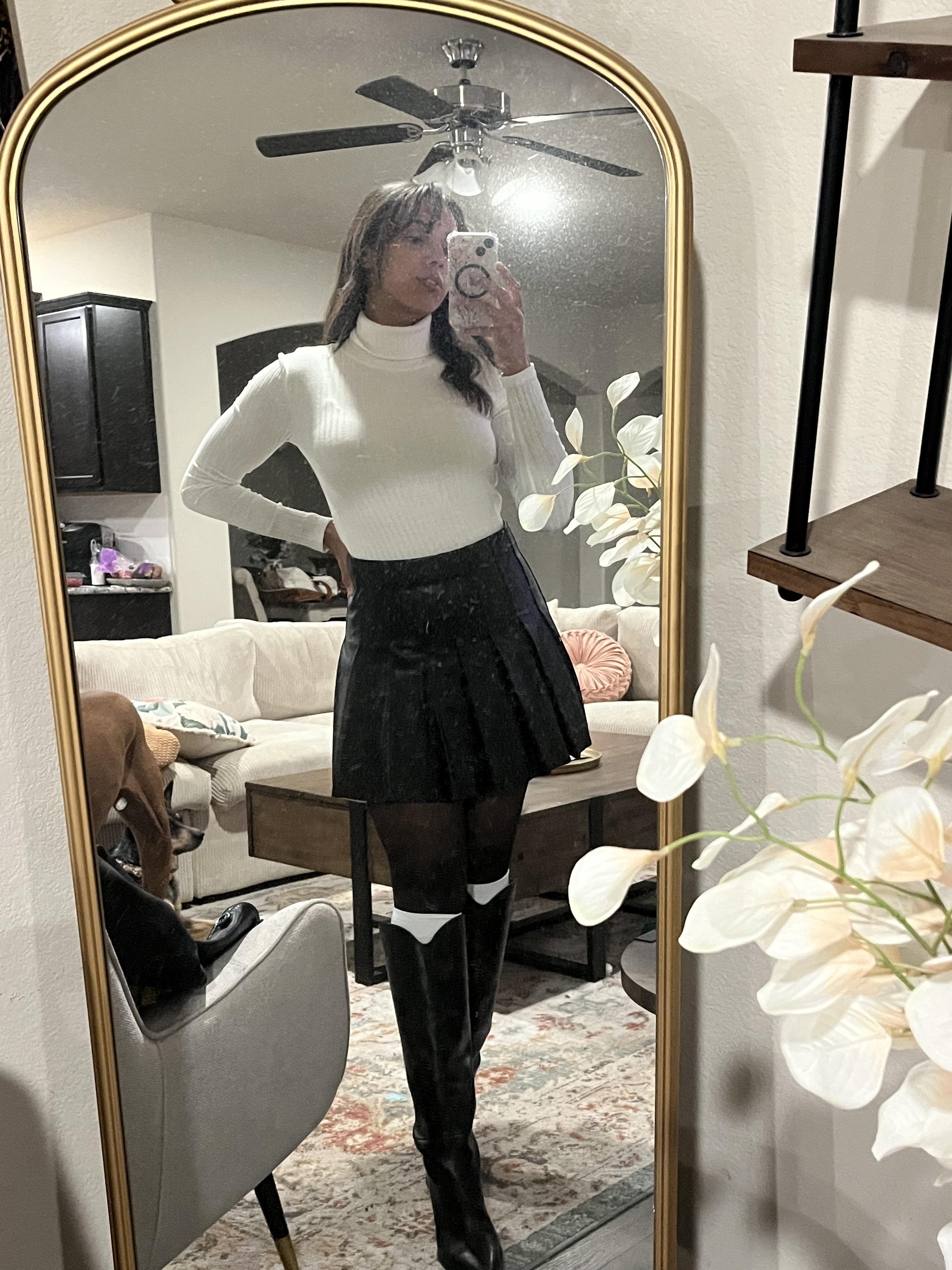 Woman in a pleated leather mini skirt and various white tops and hosiery posing for mirror selfies