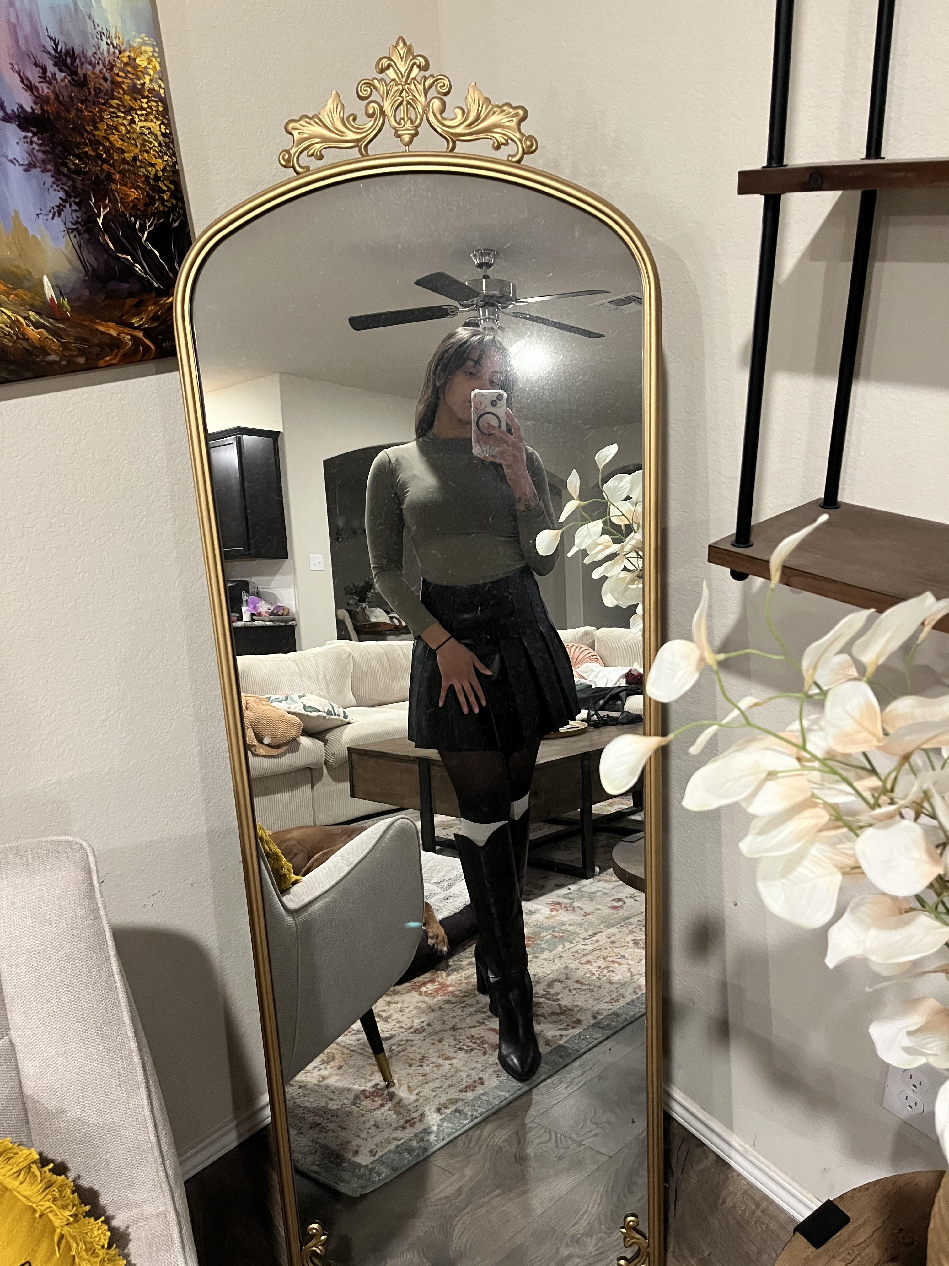 Woman in a pleated leather mini skirt and various white tops and hosiery posing for mirror selfies
