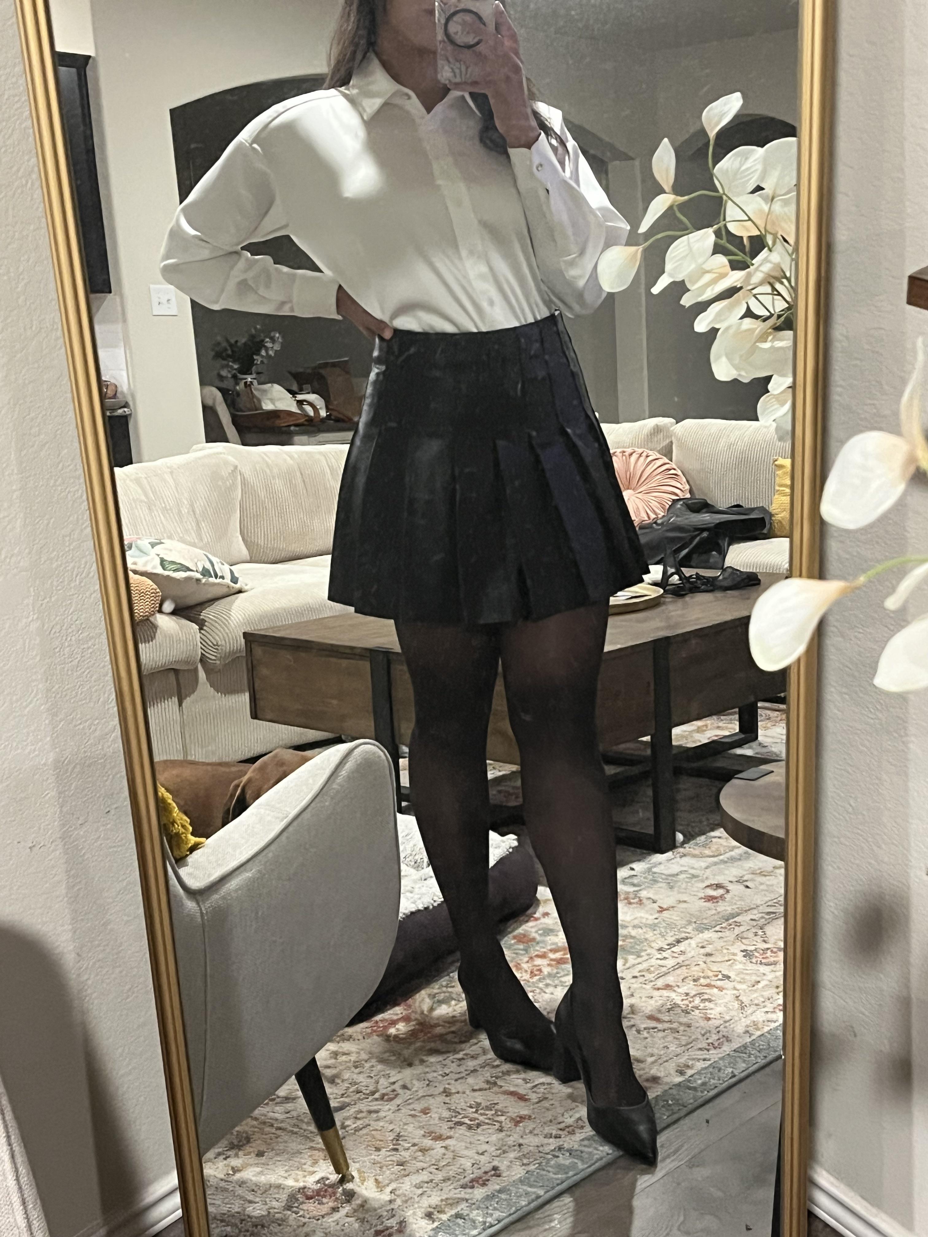 Woman in a pleated leather mini skirt and various white tops and hosiery posing for mirror selfies