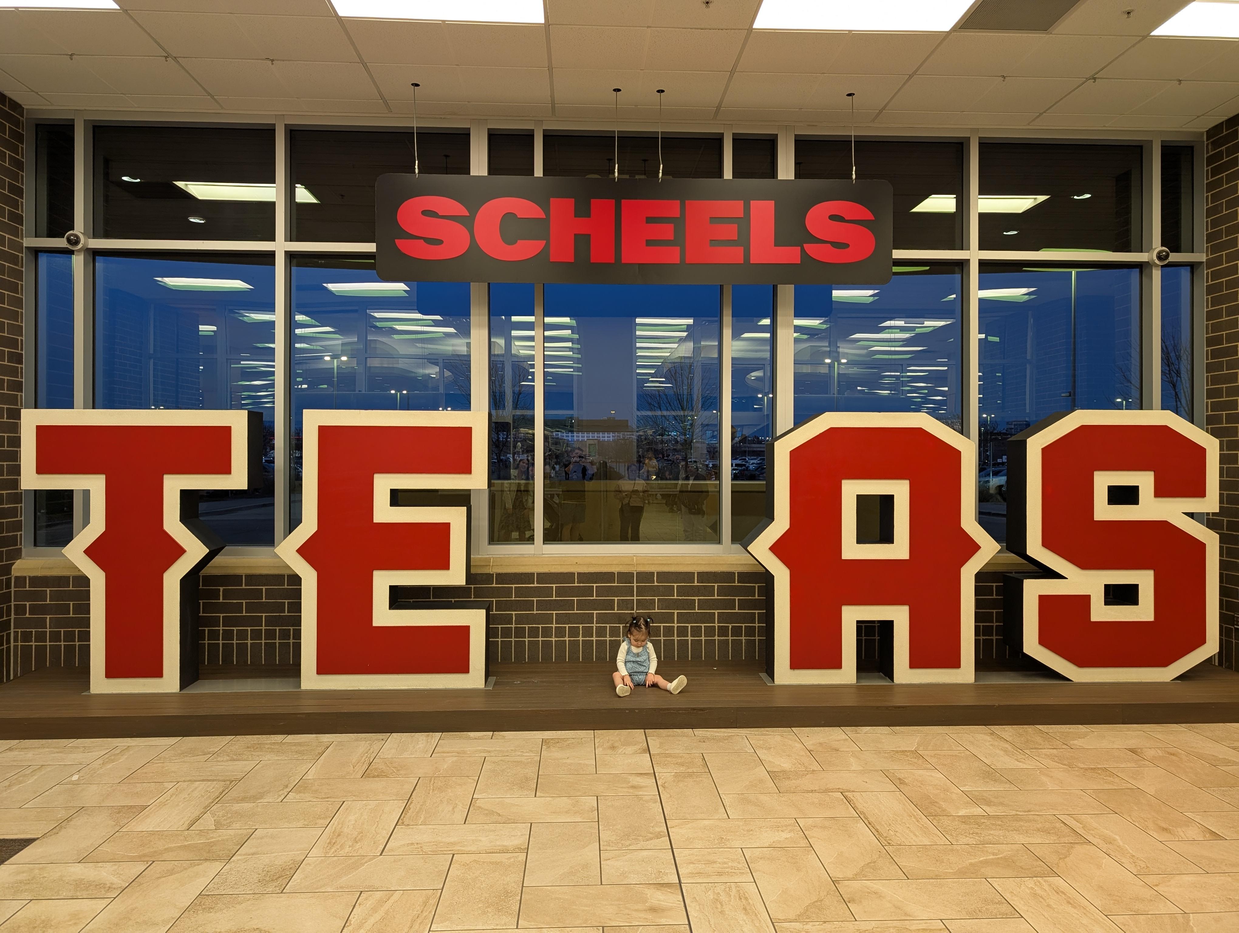 Photoshop Request of a child and man in blue jeans by a red SCHEELS sign