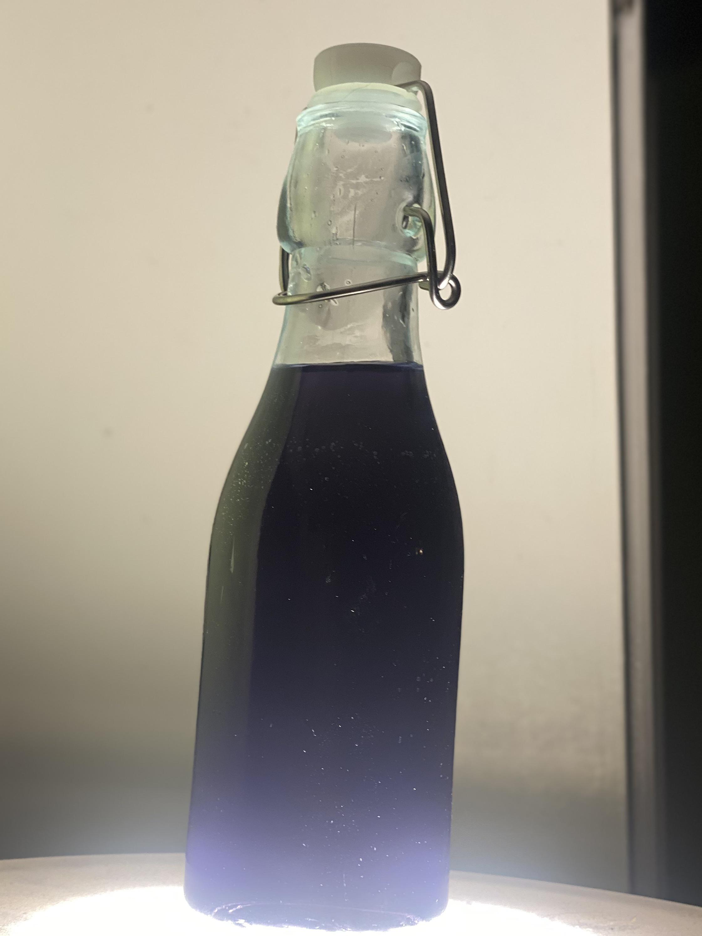 Wild violet simple syrup process from garden flowers in a metal pot to a glass bottle of purple liquid