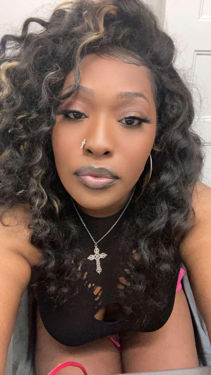 Beautiful ebony woman with long curly hair, a cross necklace, and a black cutout top