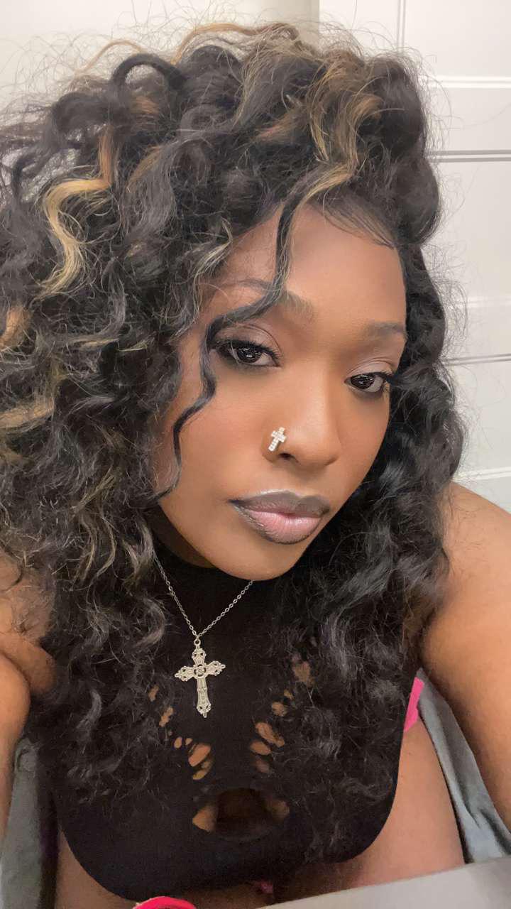 Beautiful ebony woman with long curly hair, a cross necklace, and a black cutout top