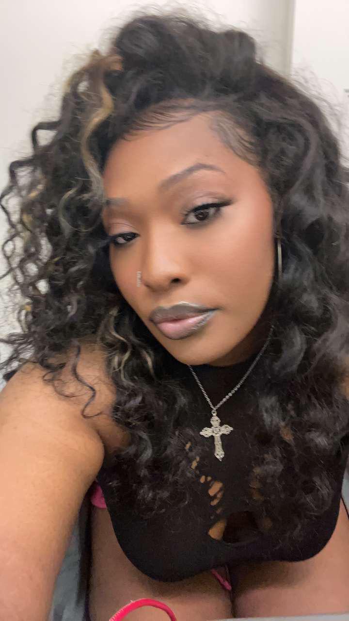 Beautiful ebony woman with long curly hair, a cross necklace, and a black cutout top