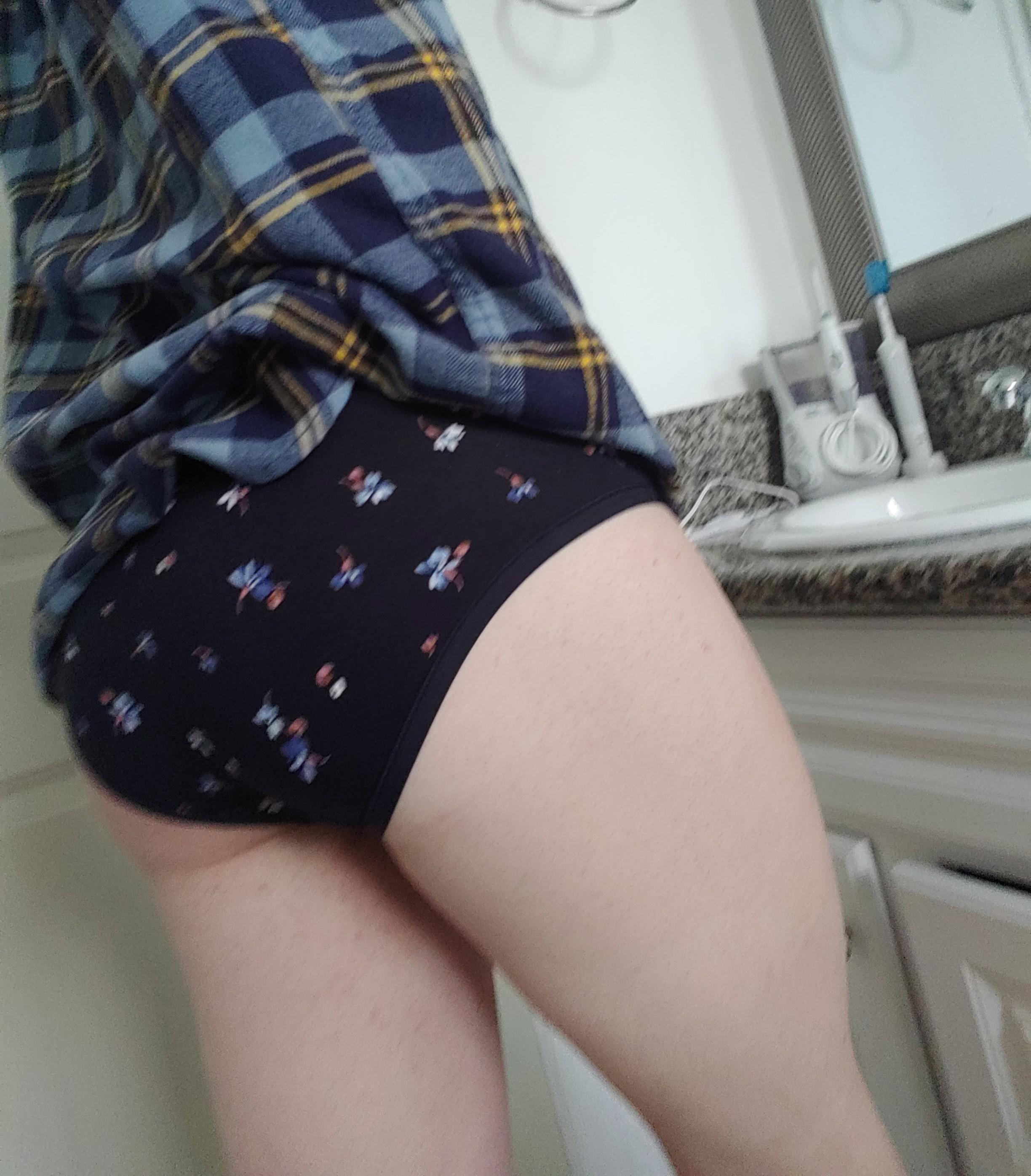 Curvy femboy in a plaid shirt and black patterned panties posing in a bathroom selfie.