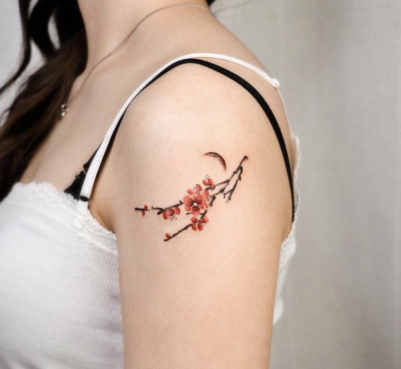 Fine line floral branch tattoo with red blossoms on the shoulder and collarbone of a person with fair skin and black hair