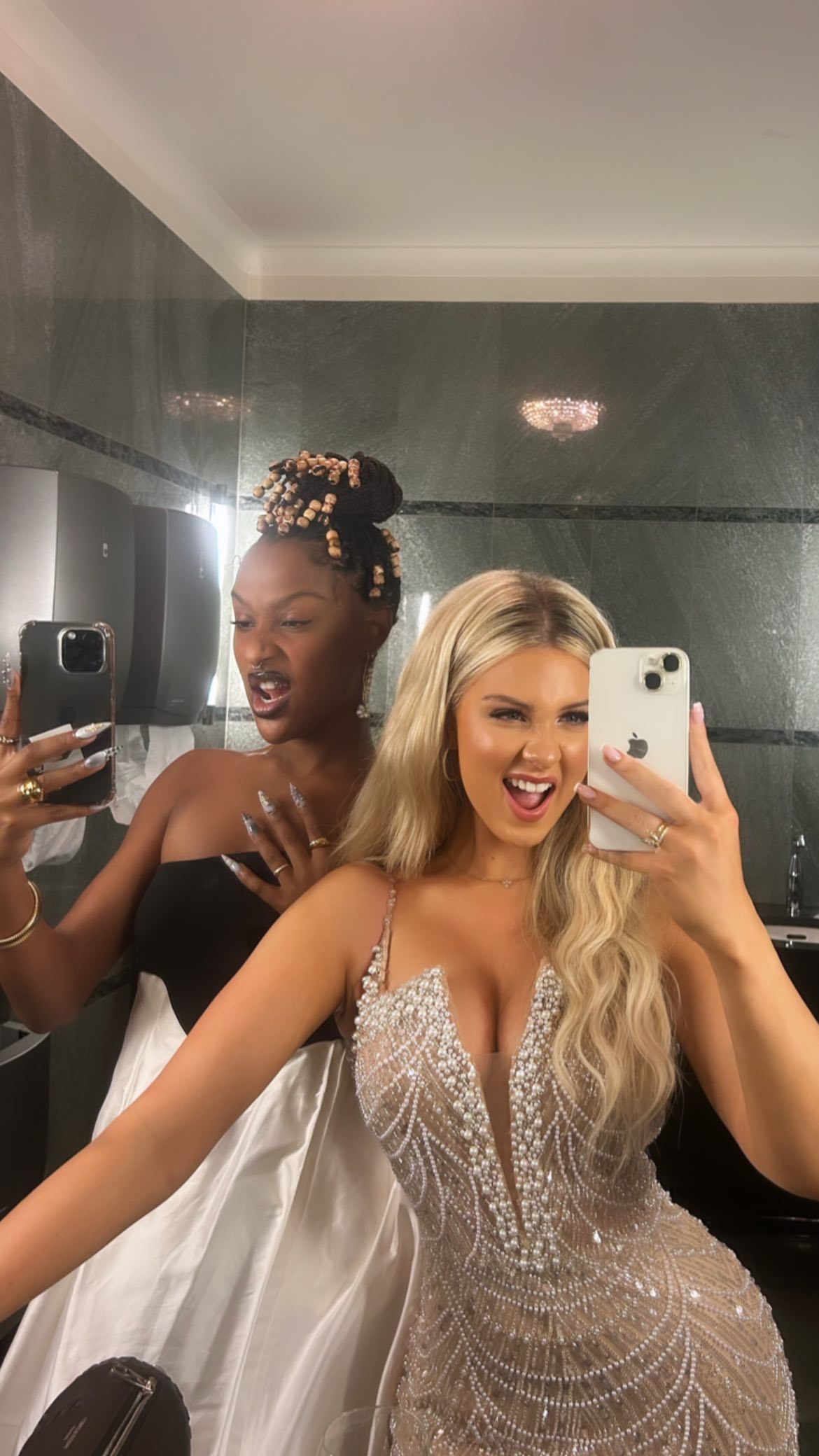 Manou Jue Cardoso and a friend taking a mirror selfie in a bathroom wearing formal evening dresses