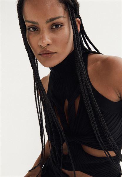 Narah Baptista in a black dress, white lace top, and grey suit, featuring her tattoos and tanned skin