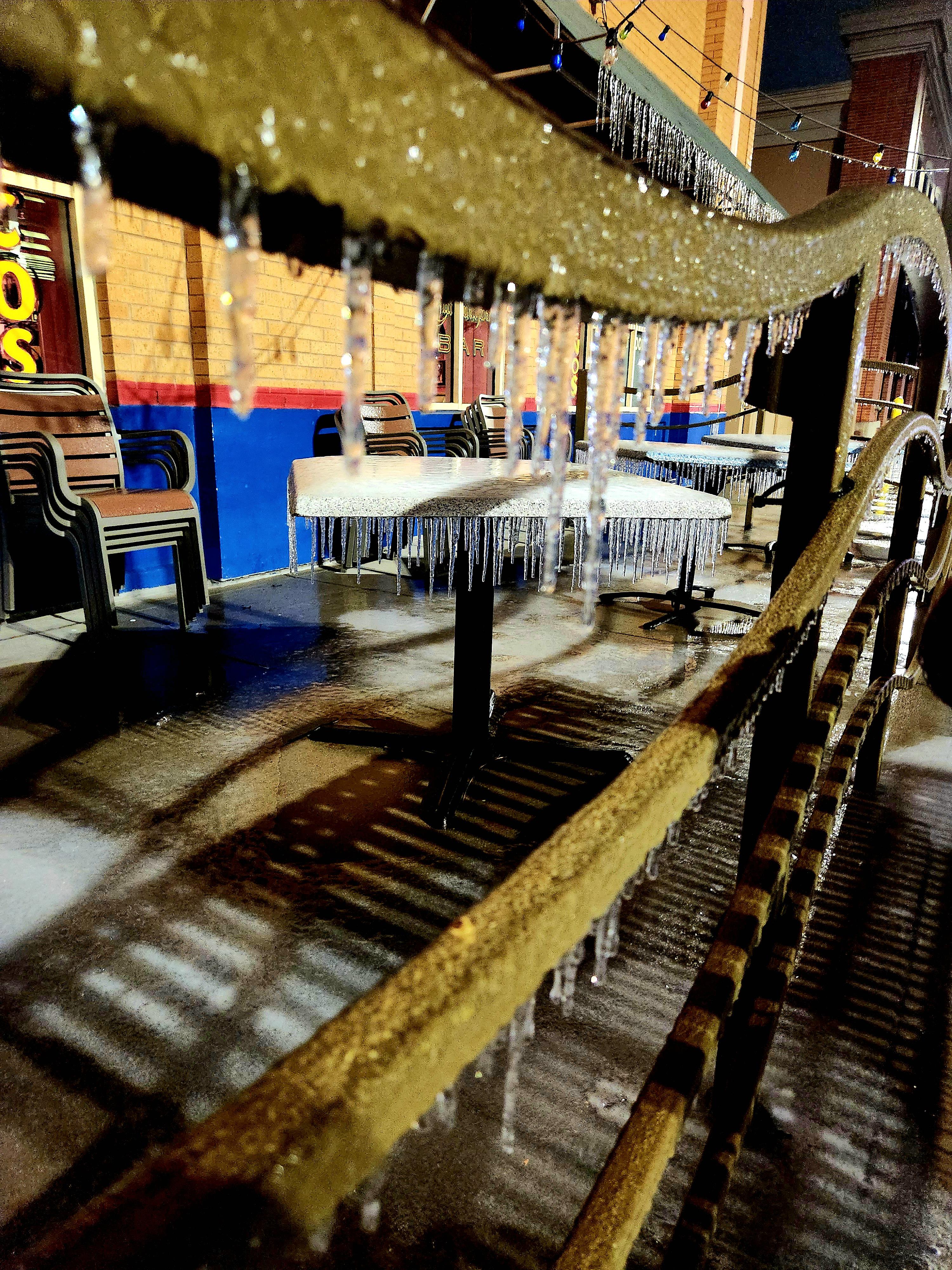 Frozen Hooters patio in Texas with ice-covered tables, chairs, and hanging icicles