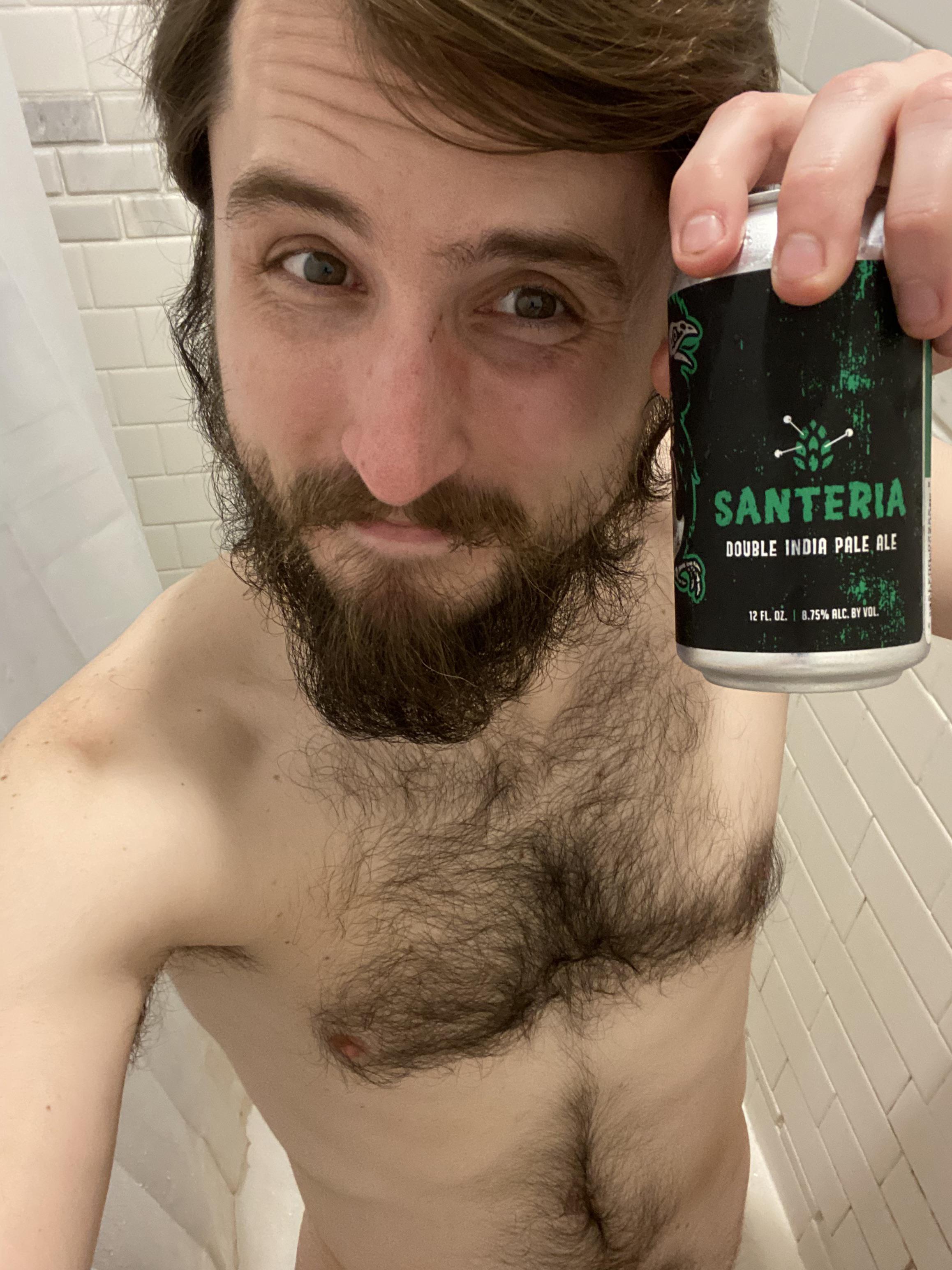 Shirtless white man with a brown beard taking a showerbeer selfie with a Santeria Double IPA can in a bathroom