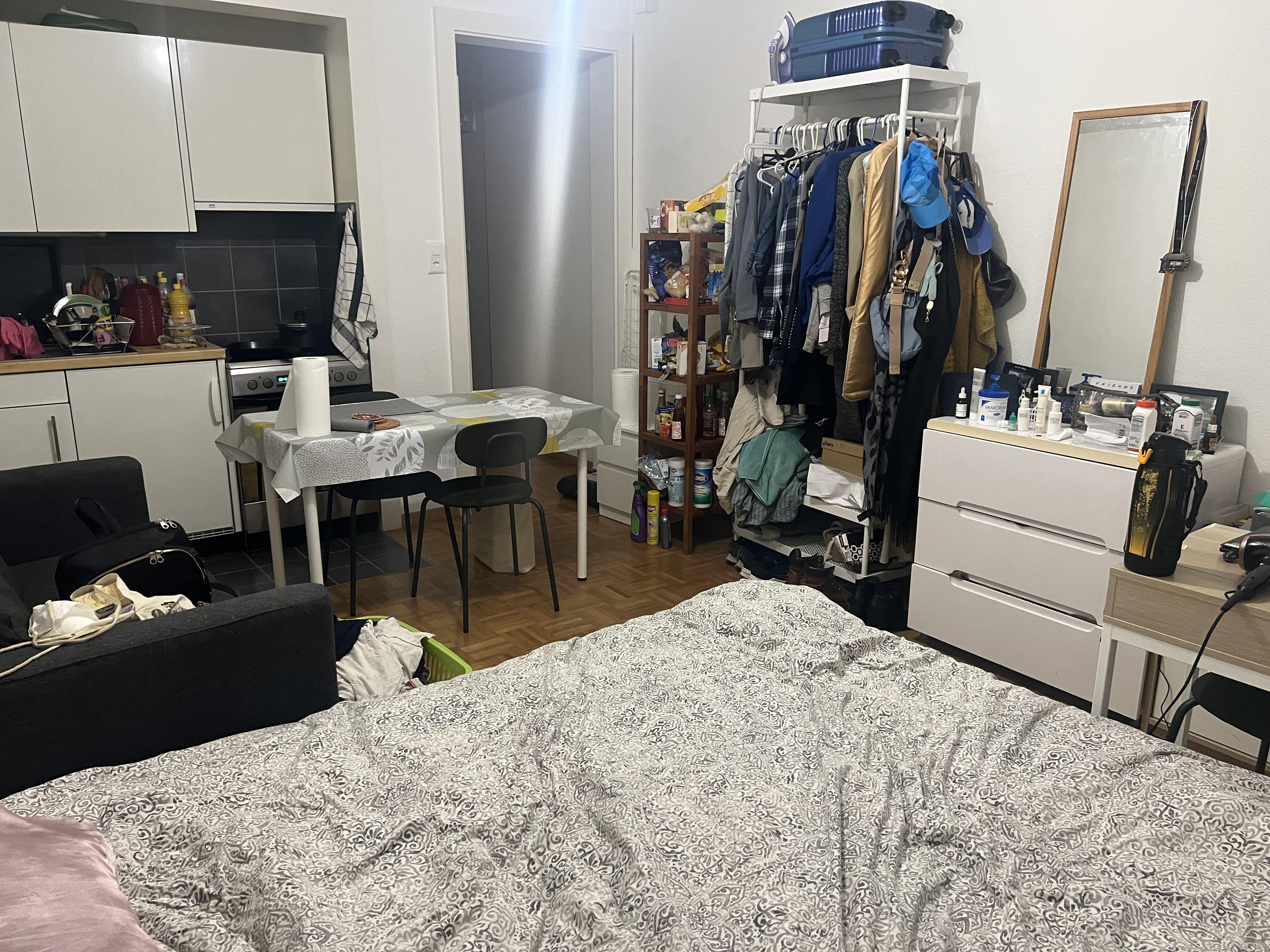 A 23sqm studio apartment with a bed, dining table, clothing rack, and kitchen area featuring floral print accents.