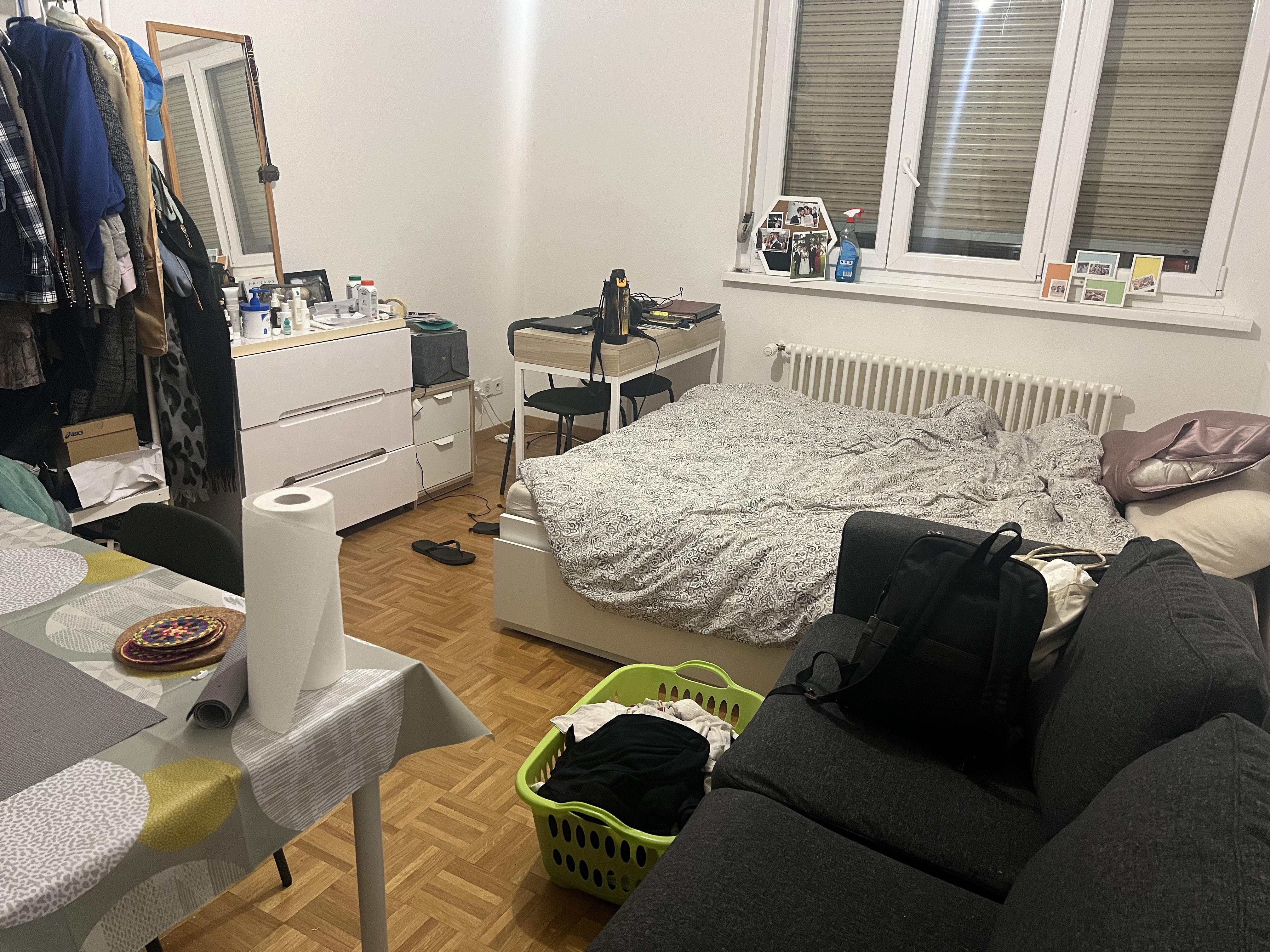 A 23sqm studio apartment with a bed, dining table, clothing rack, and kitchen area featuring floral print accents.