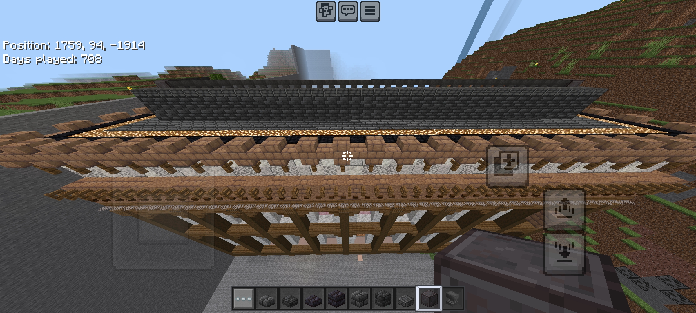 Minecraft mega build of a large wooden mansion situated among green hills and mountains.