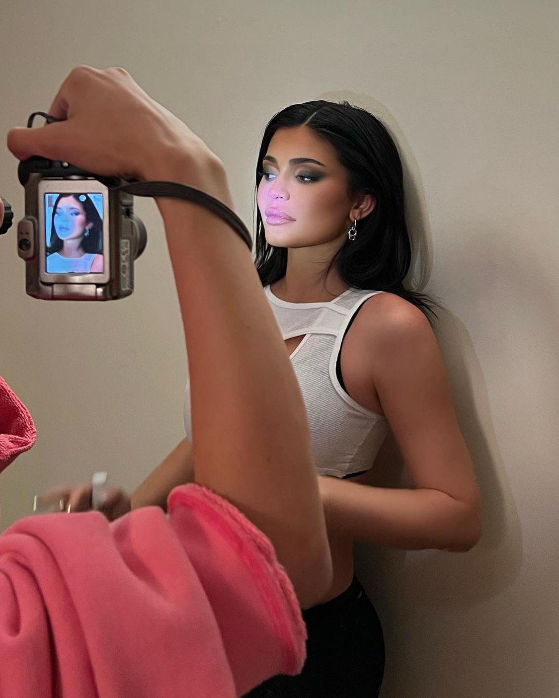 Kylie Jenner in a white cutout cropped top with black leggings and a brown halter dress.