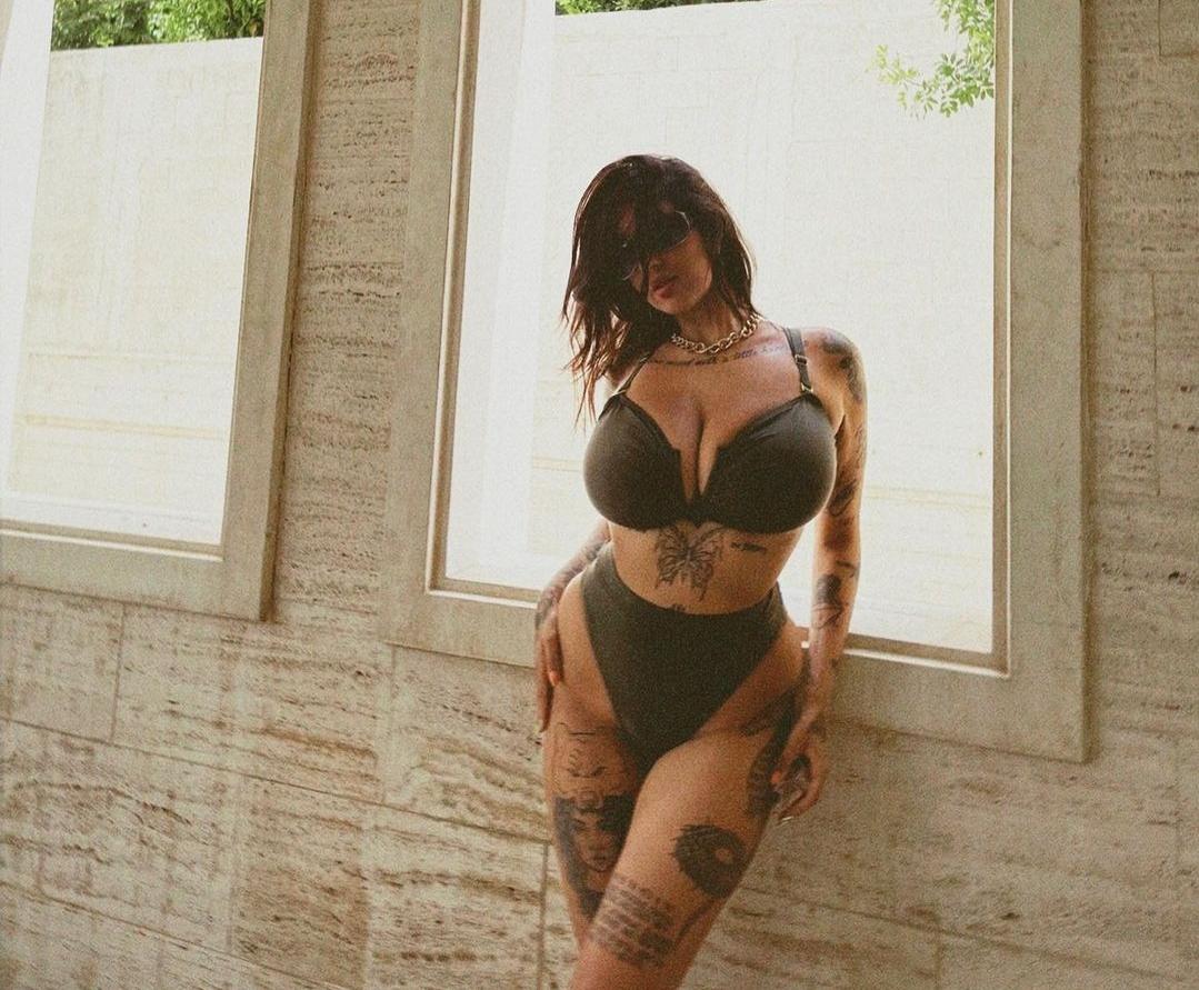 Busty mixed woman with extensive tattoos and a grey bikini posing poolside