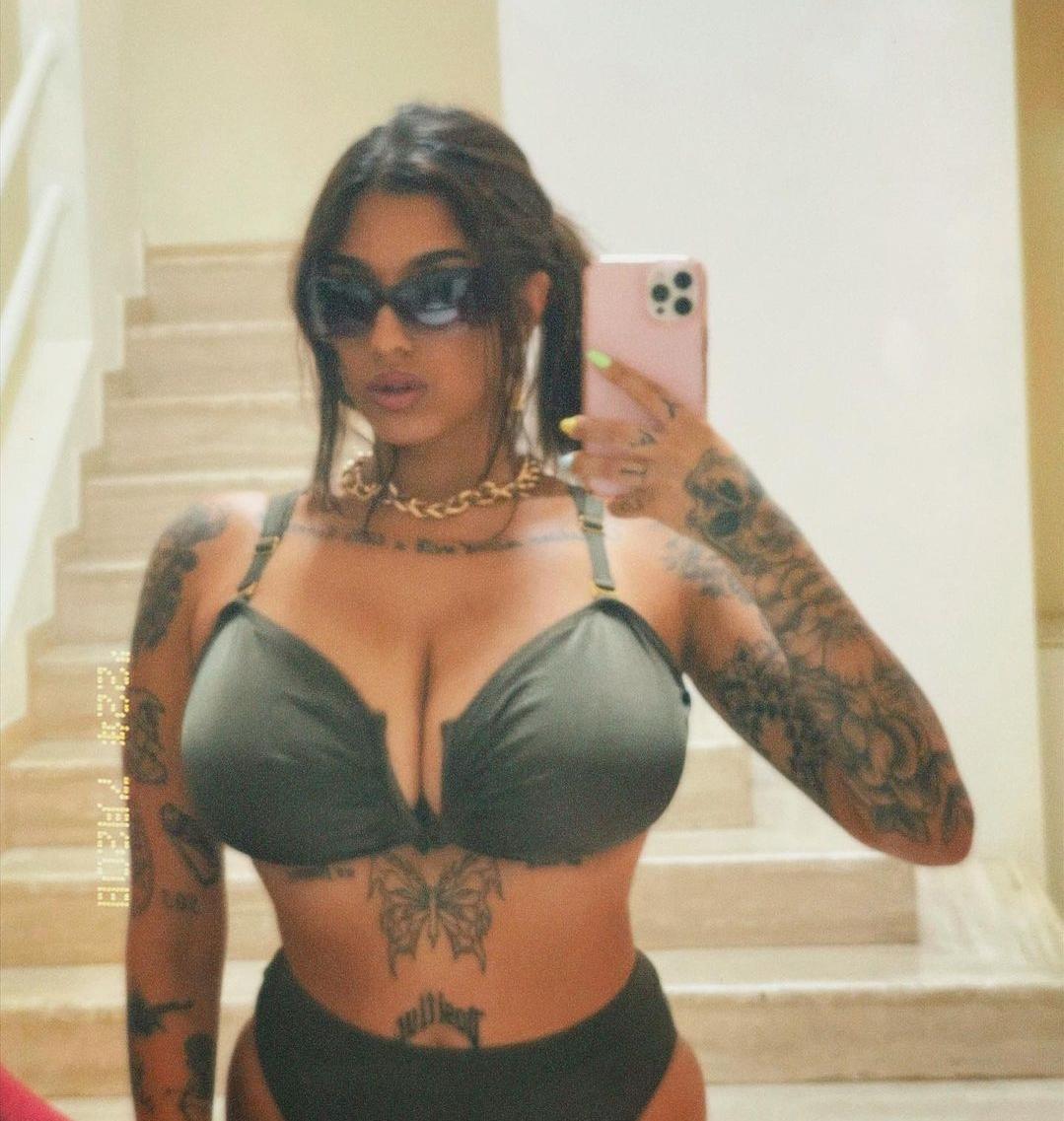 Busty mixed woman with extensive tattoos and a grey bikini posing poolside