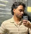 A man with natural curls taking a mirror selfie in a beige textured short-sleeved shirt.