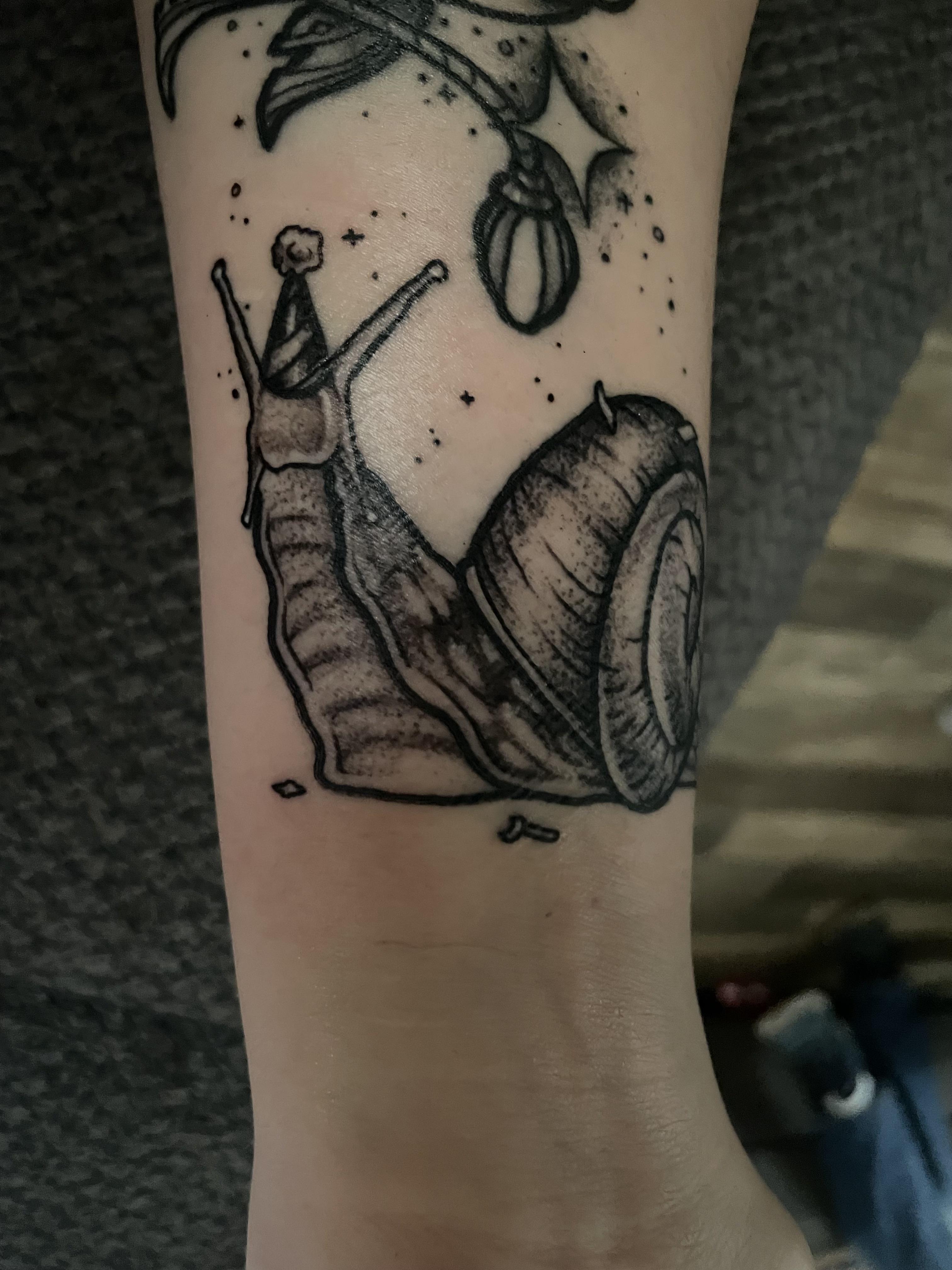 Fine line black ink tattoo of a kawaii snail with a party hat on a person's forearm