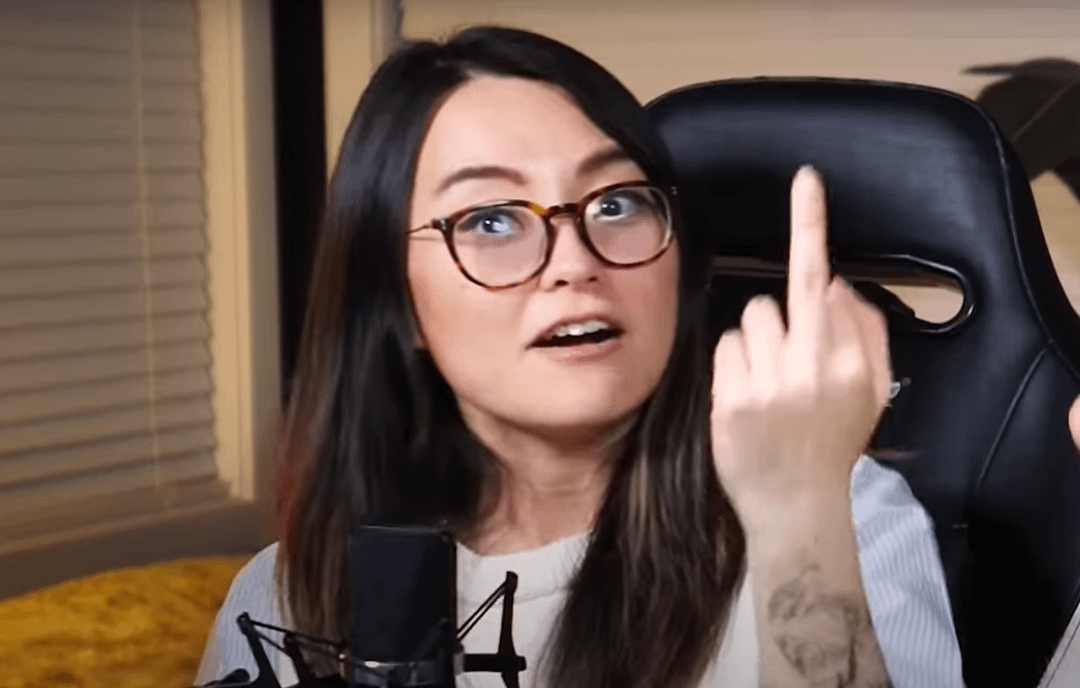 Asian egirl with glasses and a forearm tattoo giving the middle finger in a gaming chair