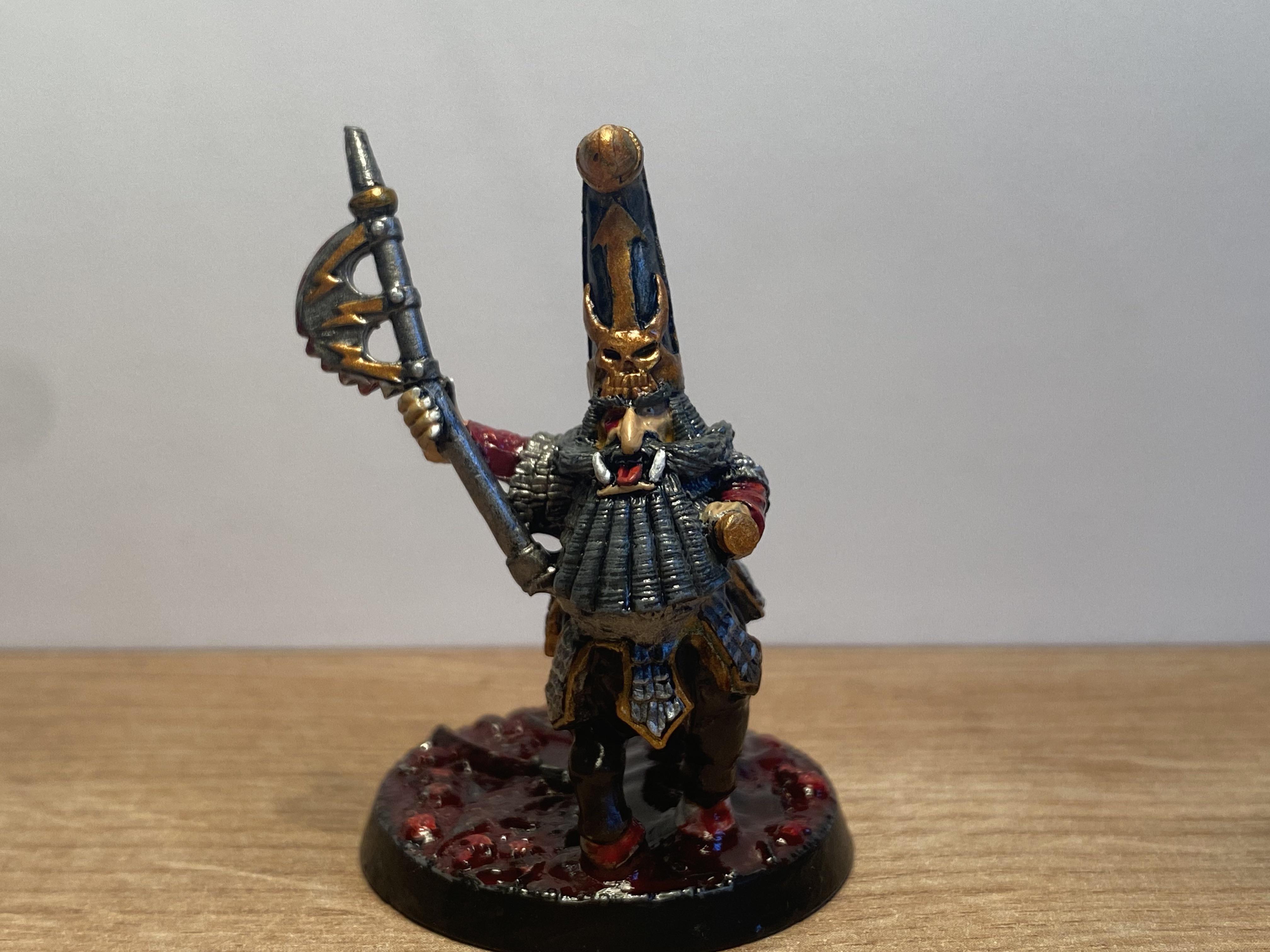 Painted Warhammer miniature of a warrior with a grey beard, tall blue and gold helmet, and an axe on a red base