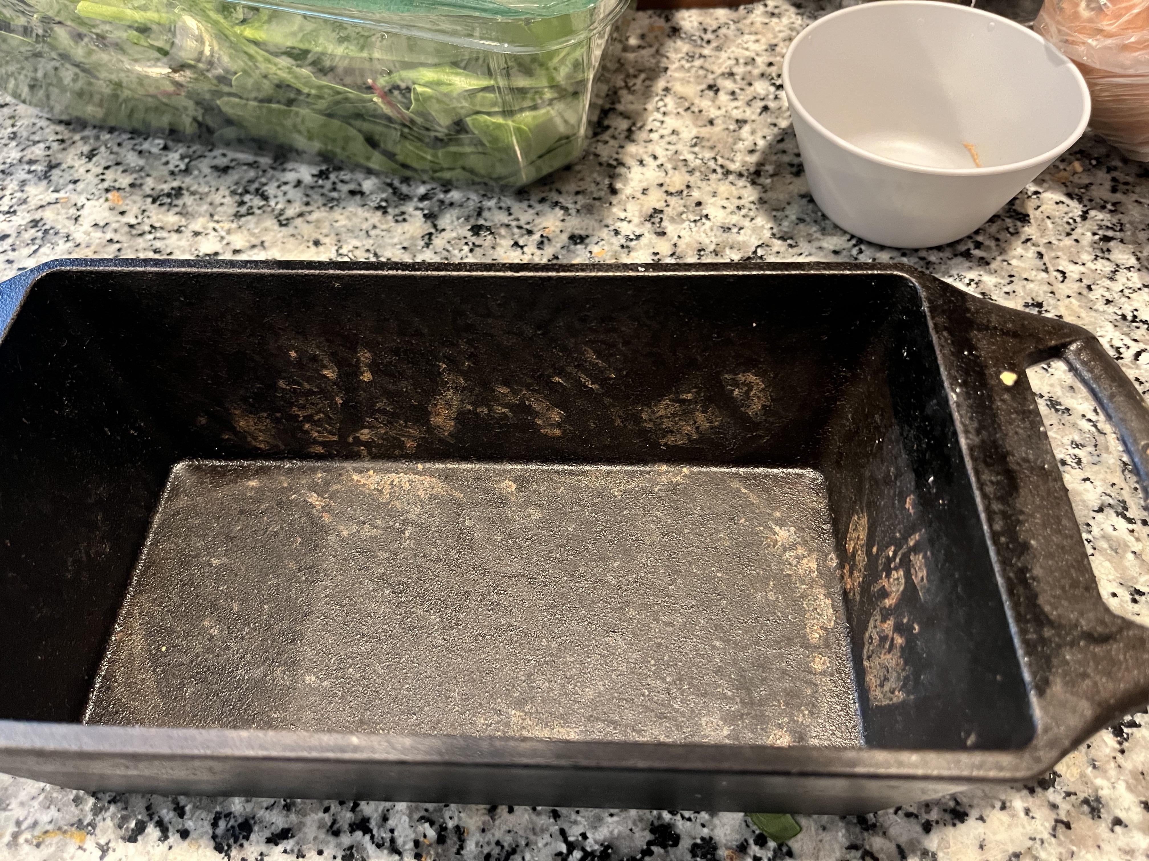Homemade bread with spots on a cooling rack next to an empty iron baking pan on a kitchen counter