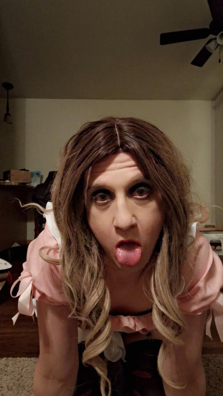 Femboy in a pink maid dress, white gloves, and checkered stockings posing for selfies with a long brown wig.