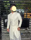 Man in a custom white patterned kurta and salwaar pants standing by a black fence