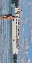 Muscular shirtless man posing in the water at Collins Beach with a large white hospital ship in the background.