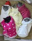 Five kittens wrapped in colorful towels like purritos lying on a brown textured surface.