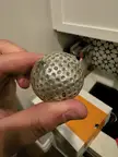 A person with pale skin holding a metallic, dimpled sphere created from a two part mold.
