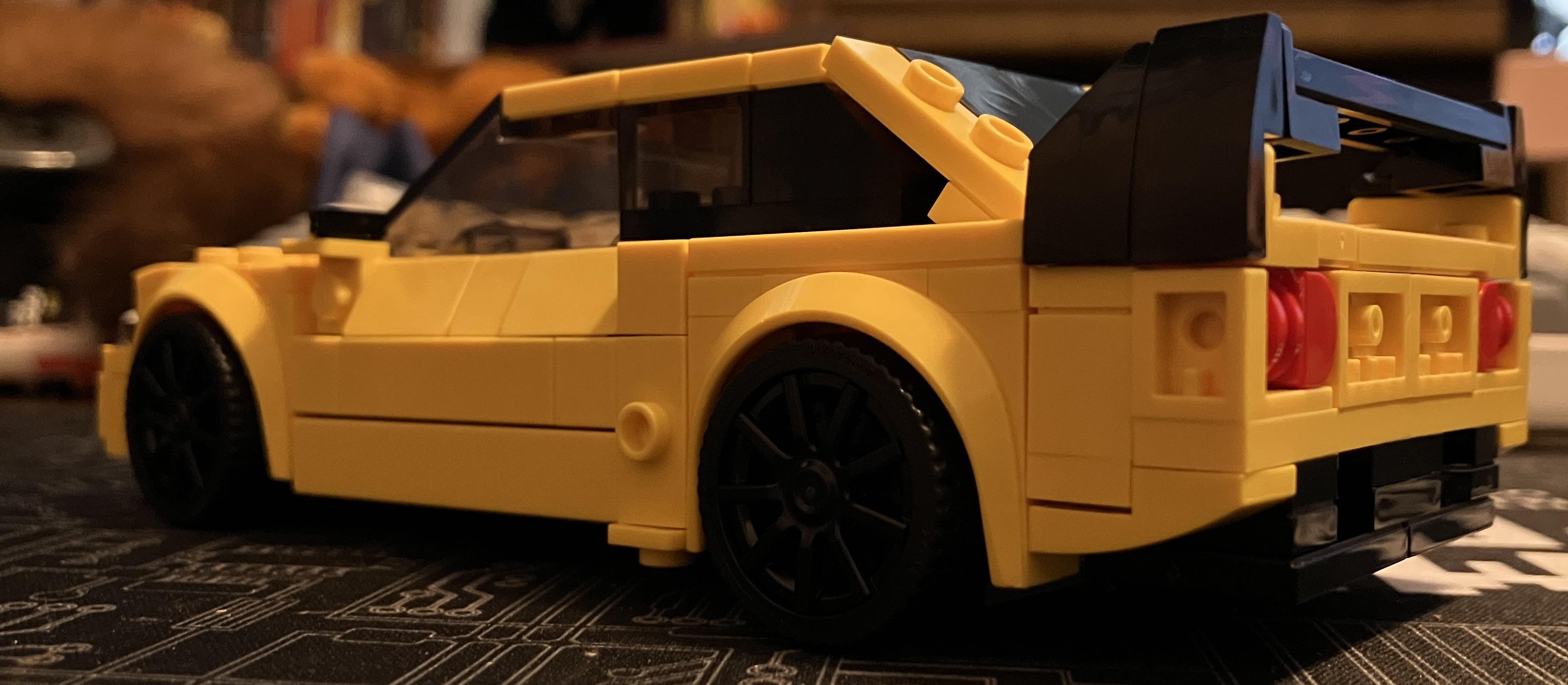 Yellow Lego Lancer sports car model on a gaming pc desk setup with a keyboard and desk mat