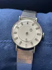 Close-up of a luxury Le Coultre watch with a diamond-marker dial and metallic band on blue fabric.