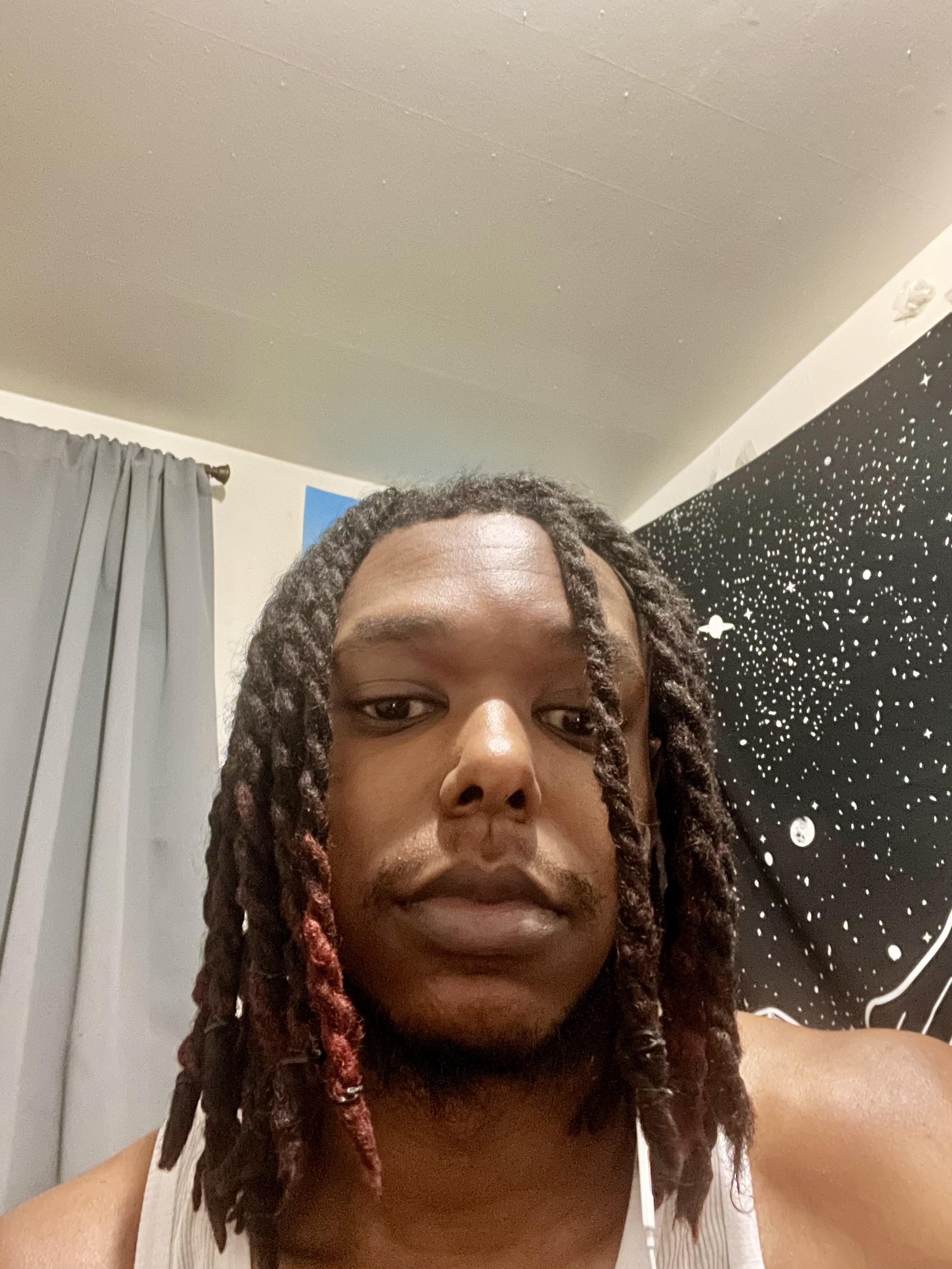 Man with long dark dreadlocks with red accents in a white tank top and grey t-shirt