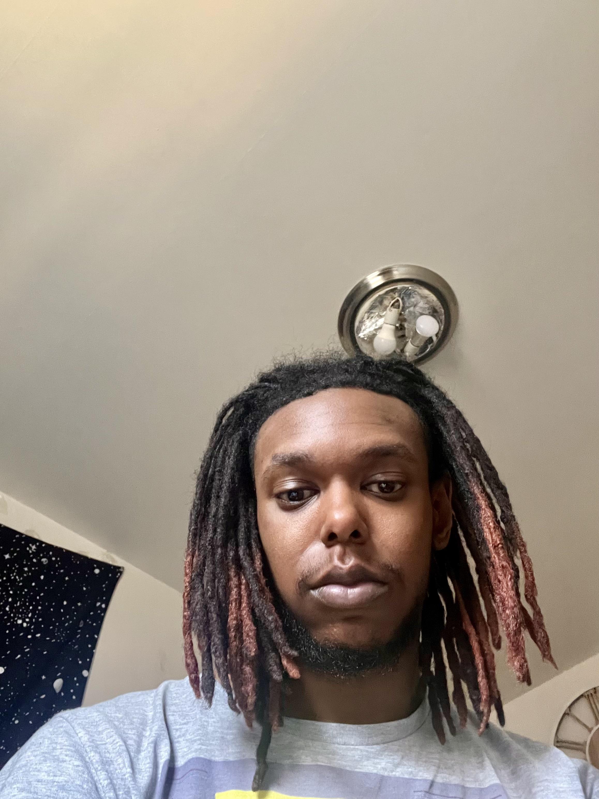 Man with long dark dreadlocks with red accents in a white tank top and grey t-shirt