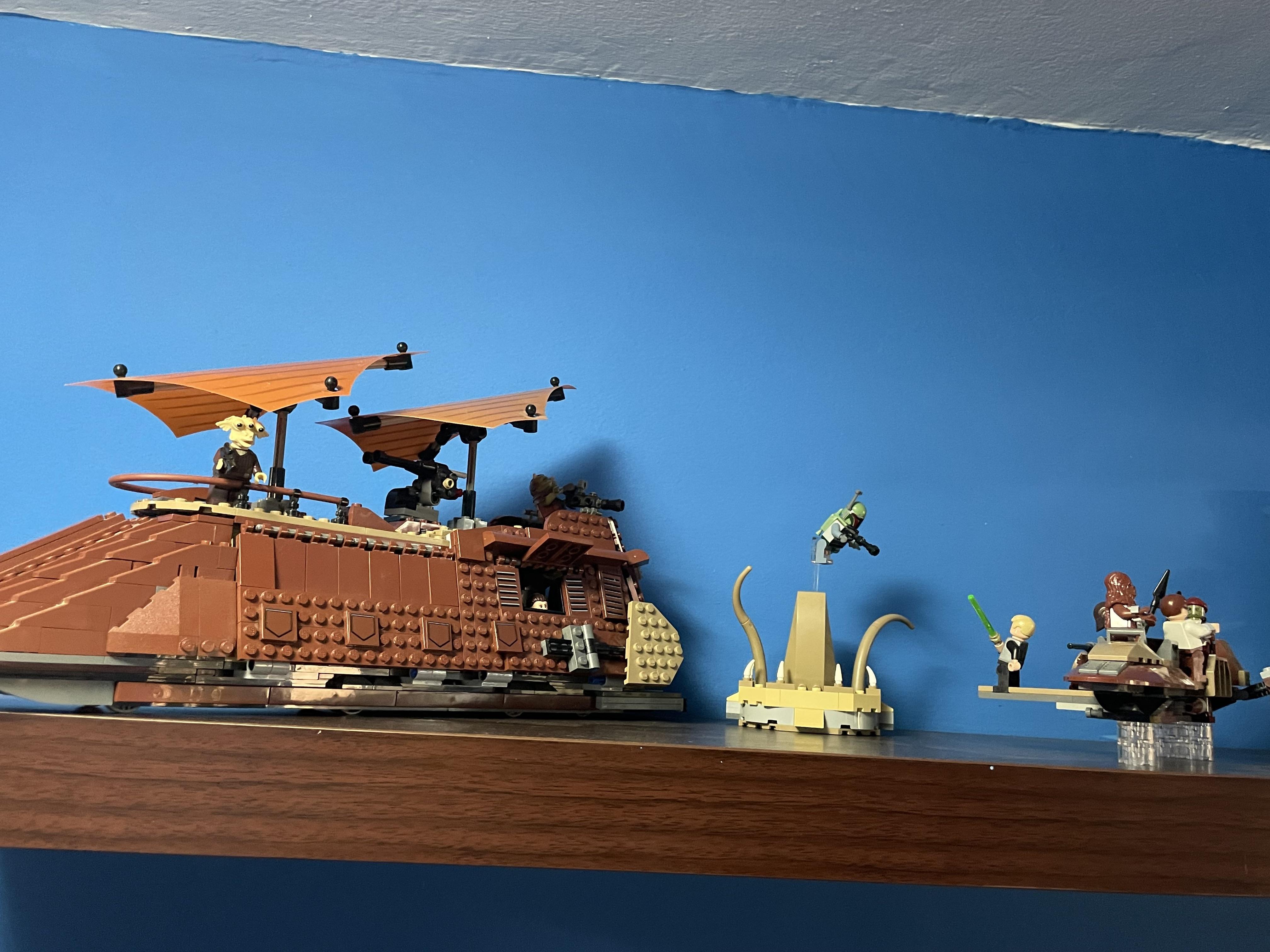 LEGO building set with minifigures and a large brown creature on a wooden shelf against a blue wall