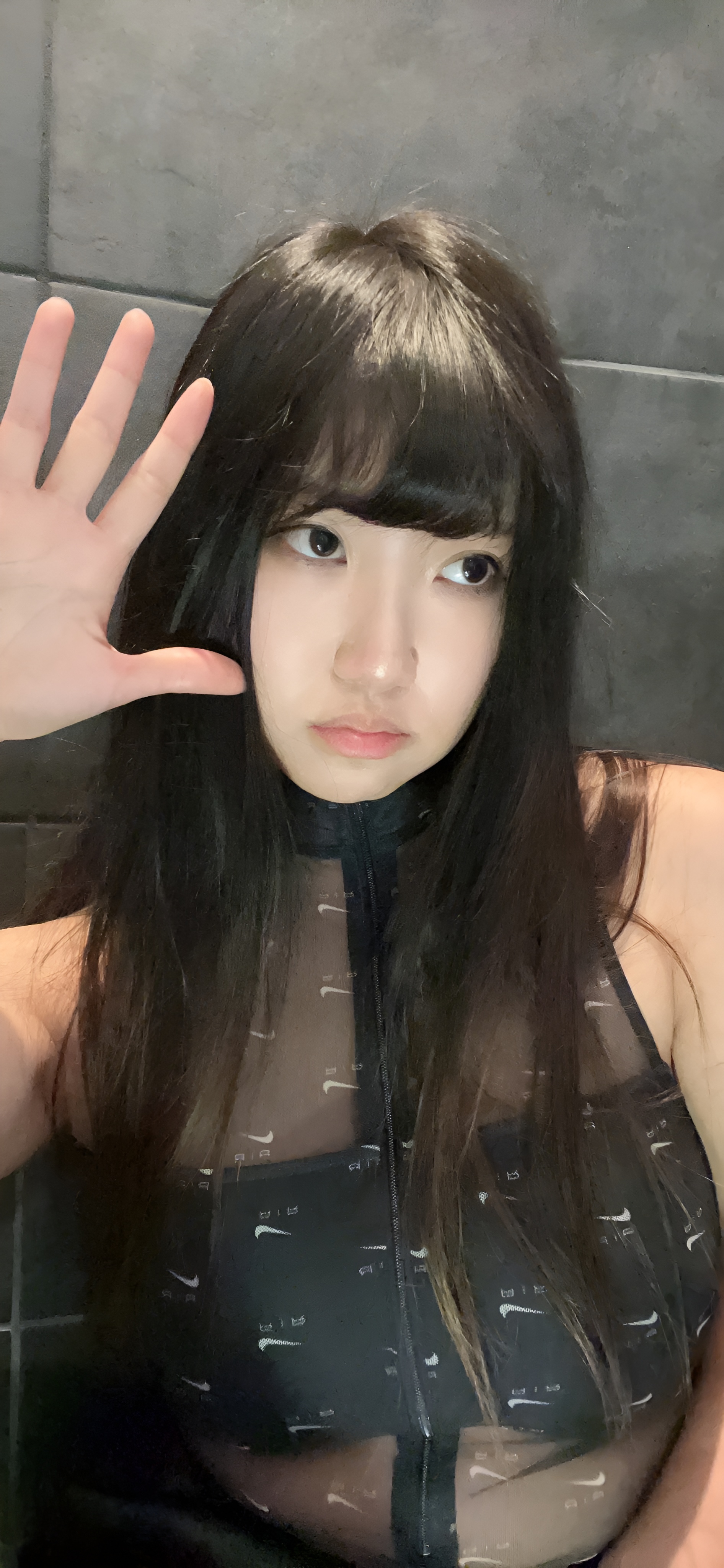 Aria wearing a black sheer top with a zipper, posing for two side-by-side selfies against a grey tiled wall.