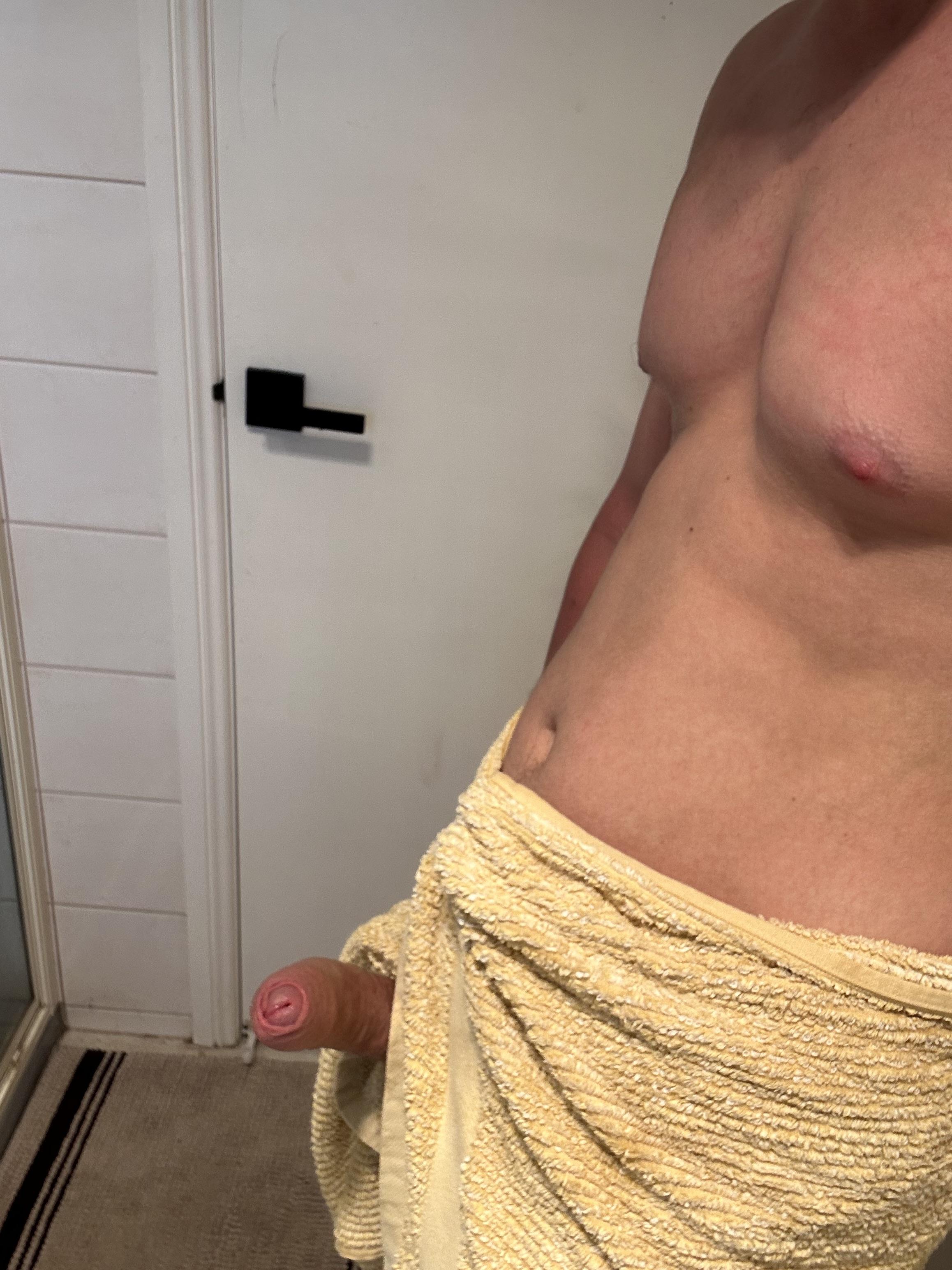Athletic white man with a fresh teendick and uncut penis posing in a yellow towel in a bathroom selfie.